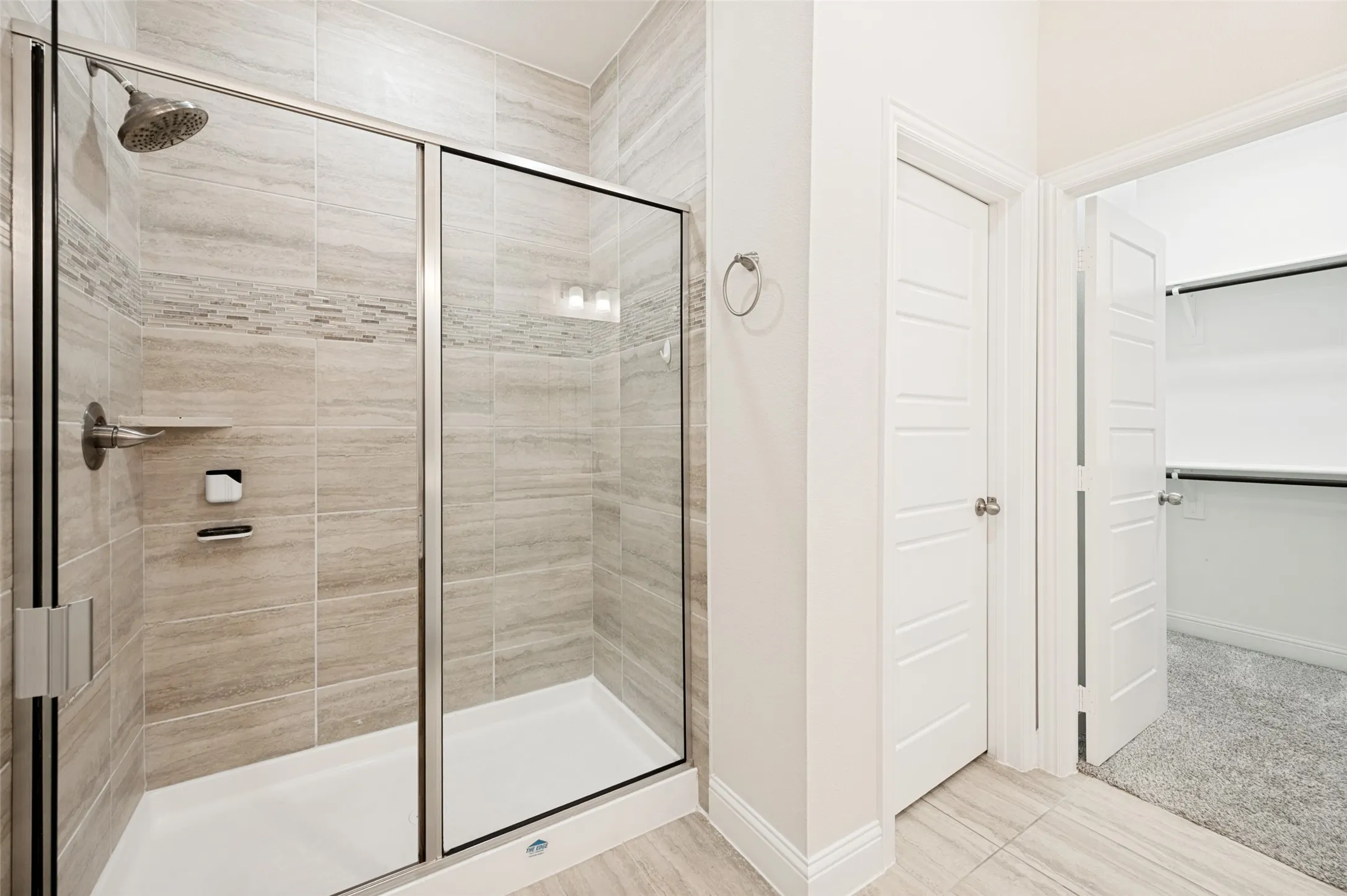 Shower enclosure with glass doors, a rainfall showerhead, and a tiled surround with decorative accents