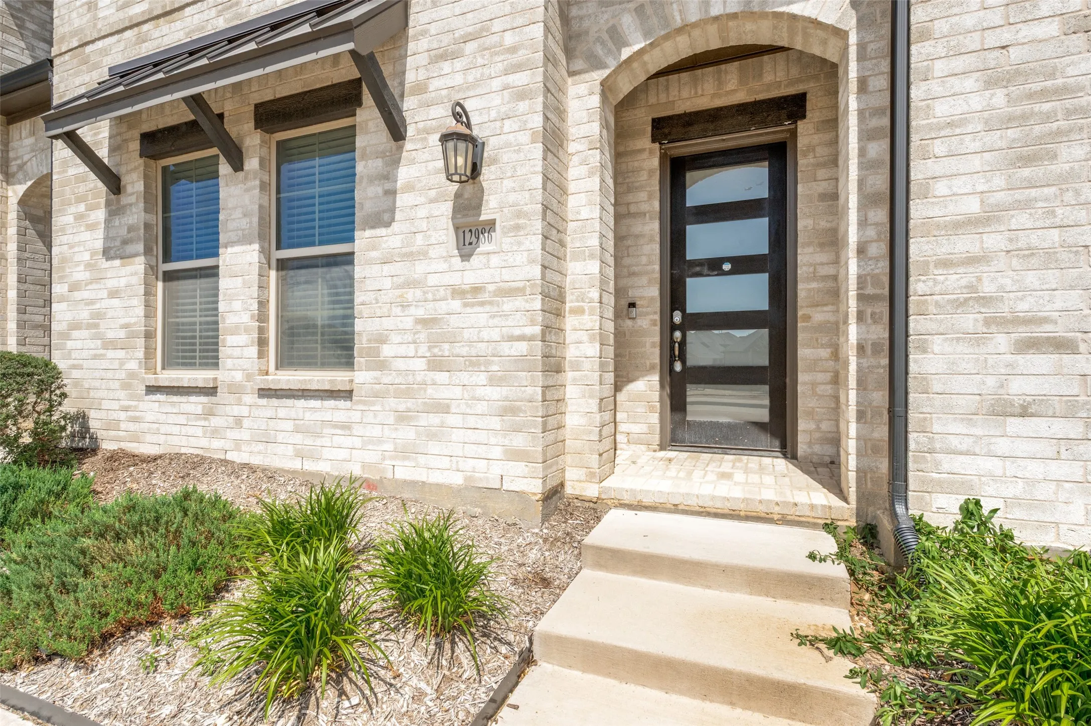 Arched entryway featuring a modern black front door with frosted glass panels, surrounded by light-colored brick masonry