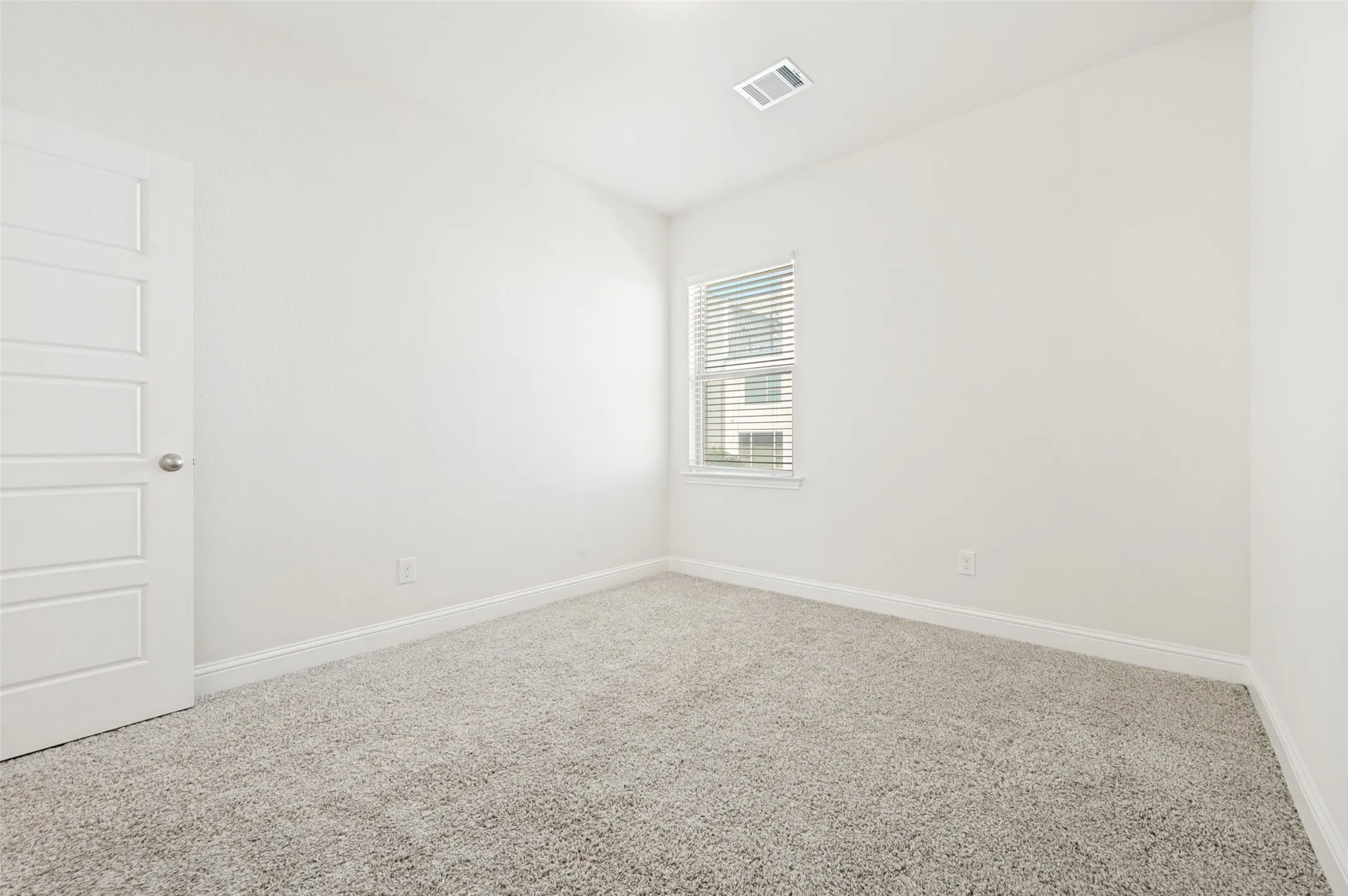 Bright room featuring light-colored carpeting, white baseboards, and a window with horizontal blinds