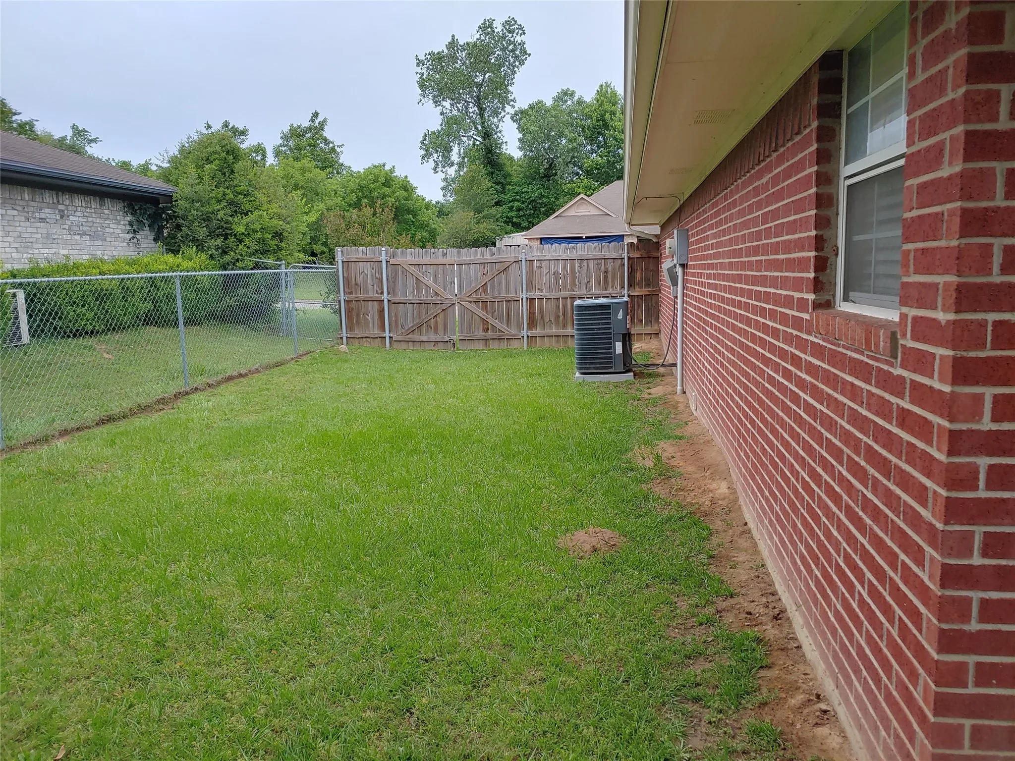 Expansive green space featuring chain link and wood fencing, a red brick exterior, and an air conditioning unit