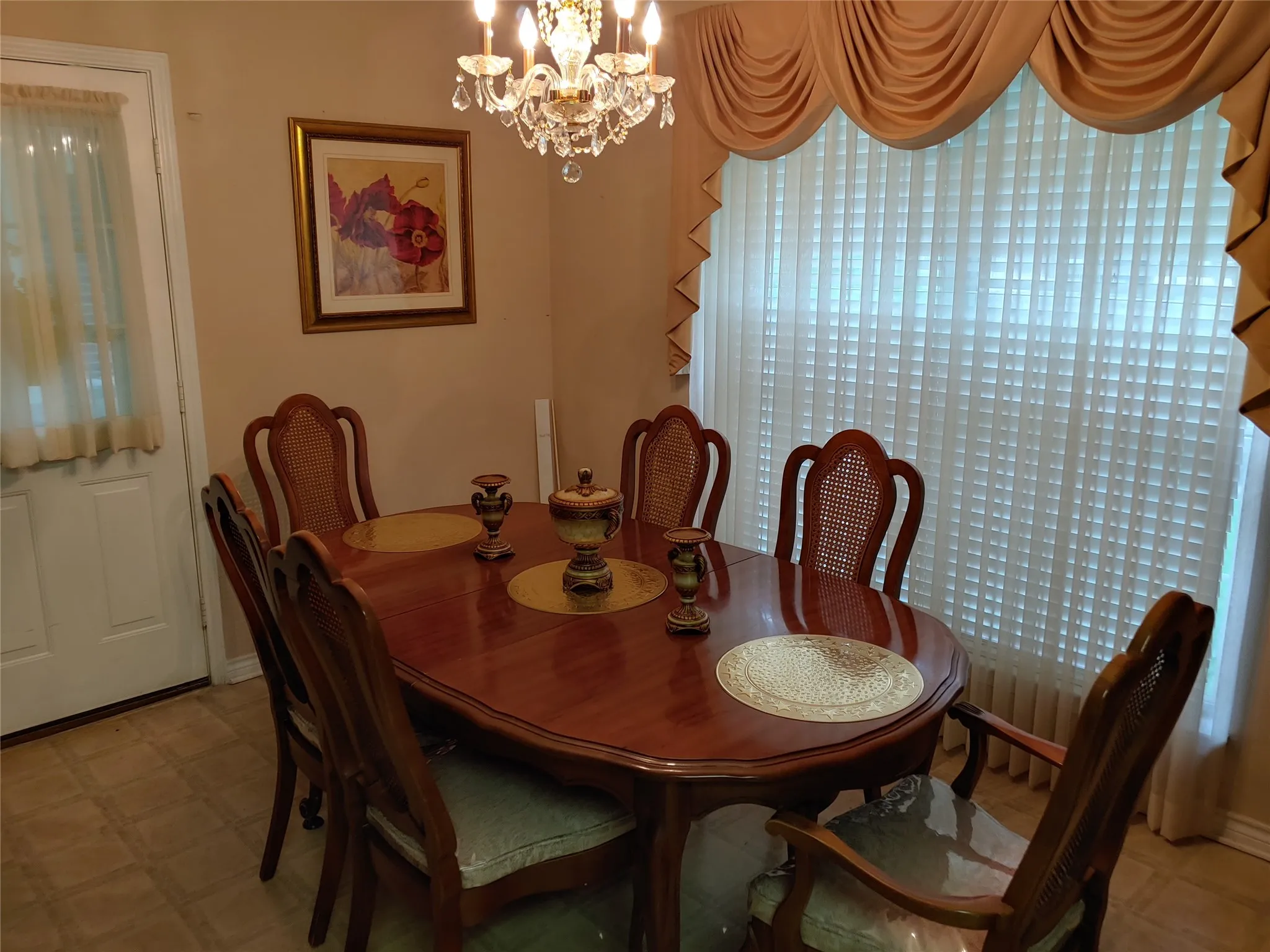 Formal dining space featuring a polished wood-finish table, a crystal chandelier, vertical blinds, and patterned flooring