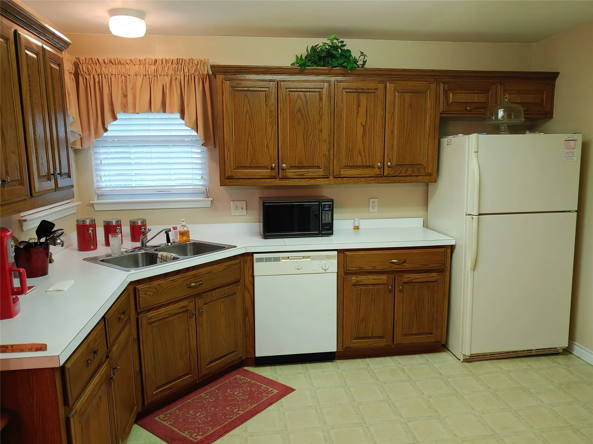 Kitchen featuring wood-finish cabinetry, white countertops, a double basin stainless steel sink, and patterned vinyl flooring