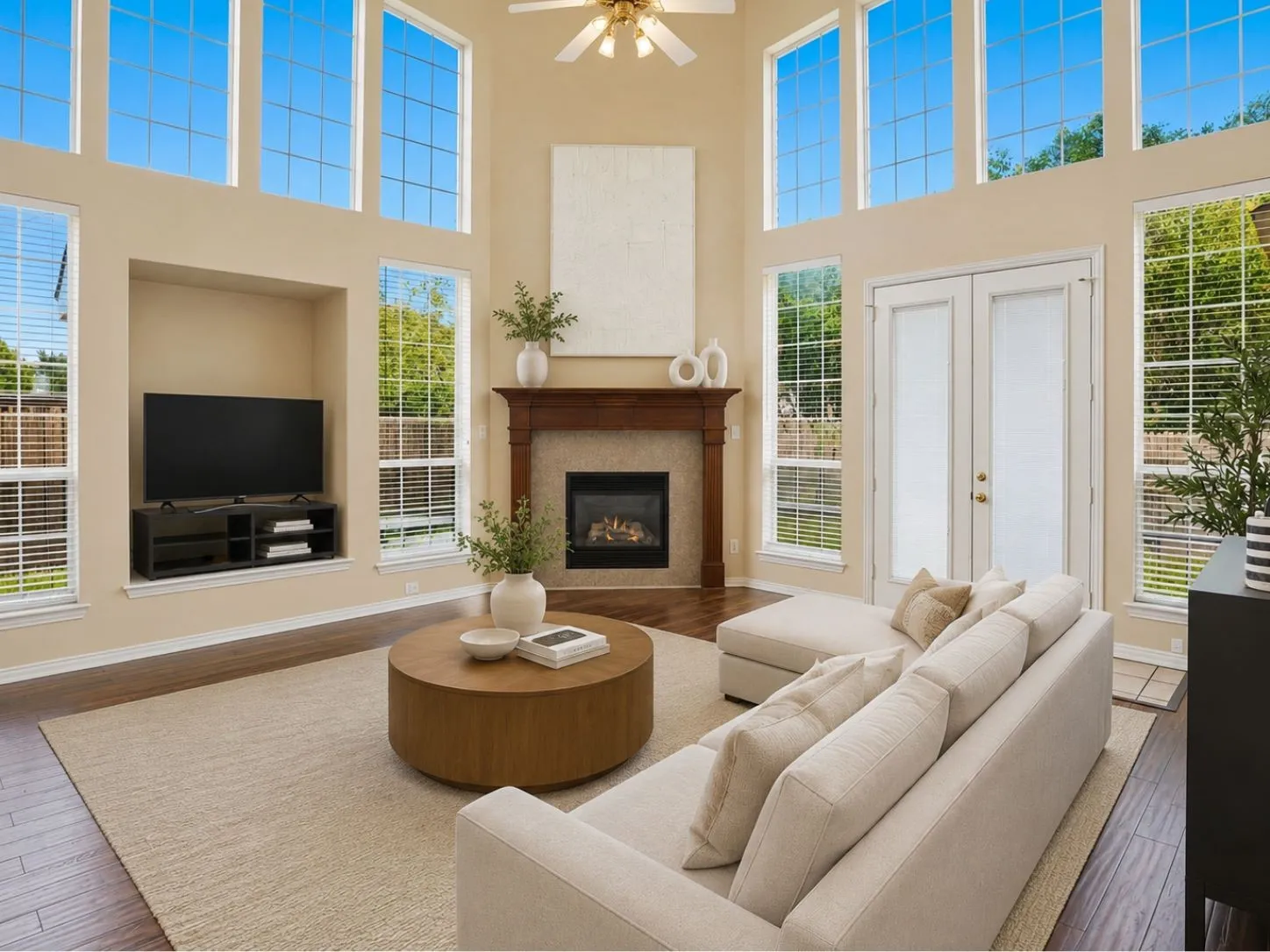 Natural light pours through two-story windows, highlighting the striking fireplace and open-concept design that makes everyday living and entertaining feel effortlessly connected.