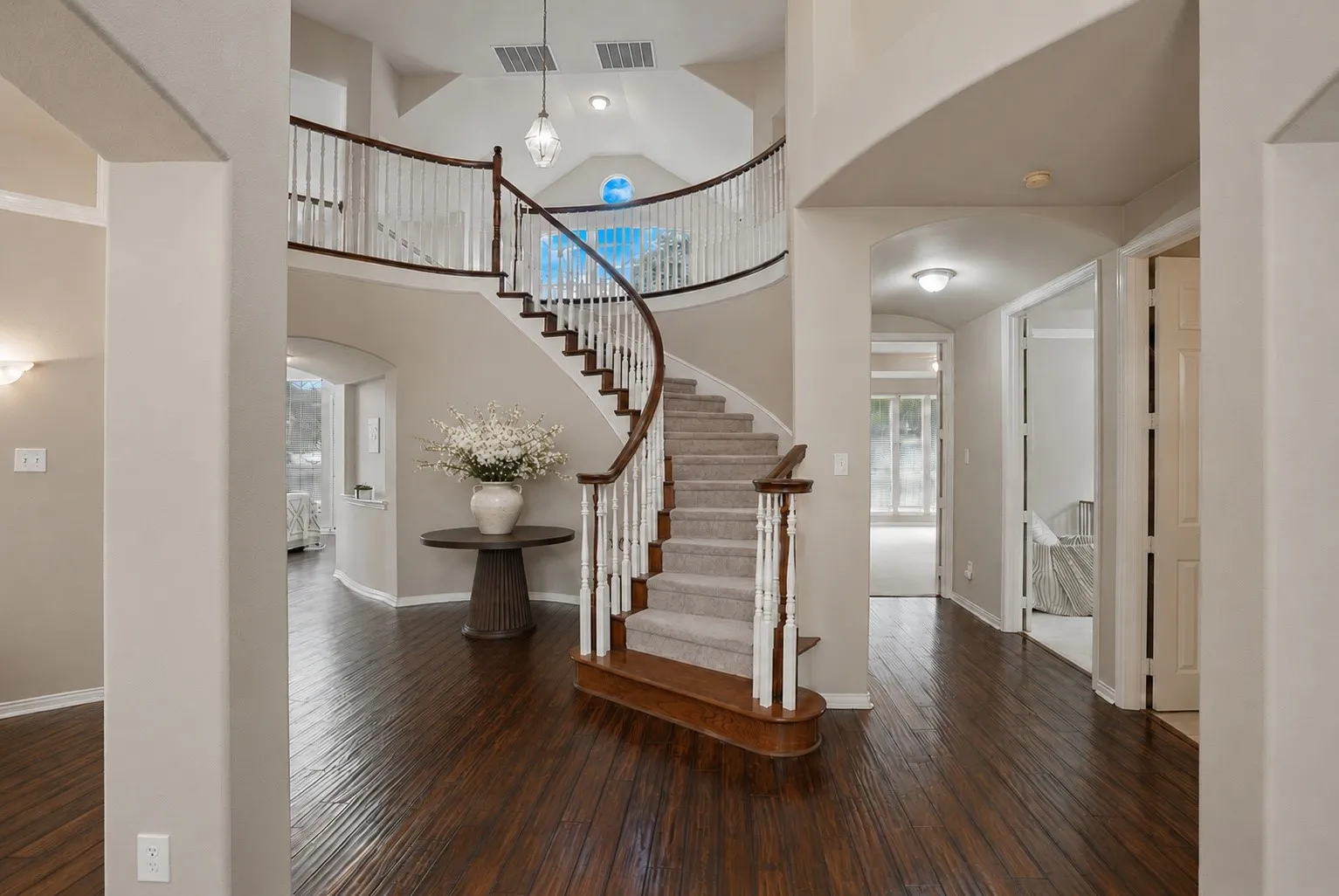 A grand entrance with a sweeping curved staircase, soaring ceilings, and rich hardwood flooring introduce a floor plan designed to impress while creating an elegant transition into the heart of the home.