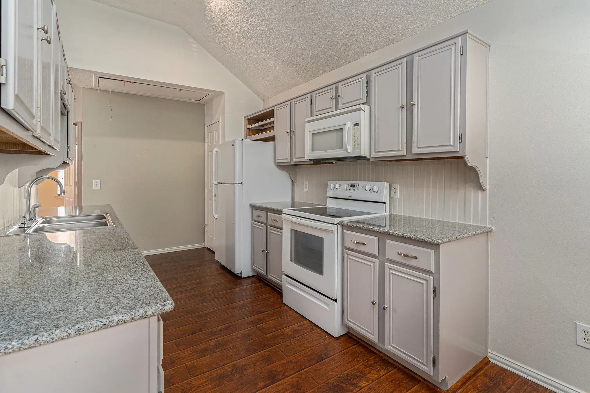 Kitchen with dark wood-style flooring, baseboards, gray cabinets, white appliances, and a sink