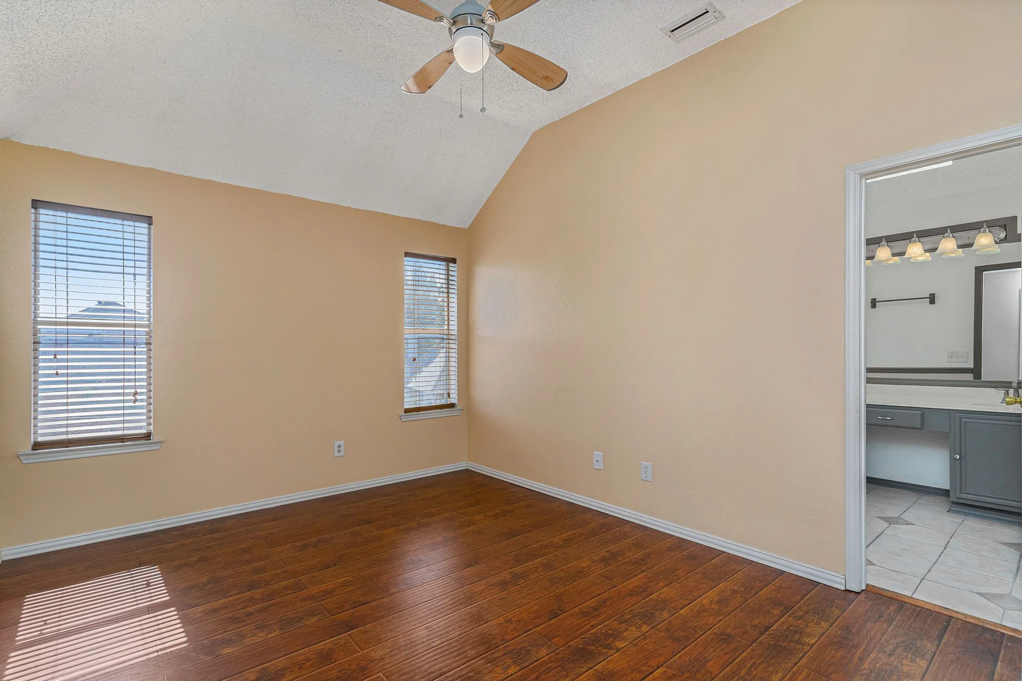 Unfurnished bedroom featuring a textured ceiling, visible vents, wood-type flooring, lofted ceiling, and baseboards