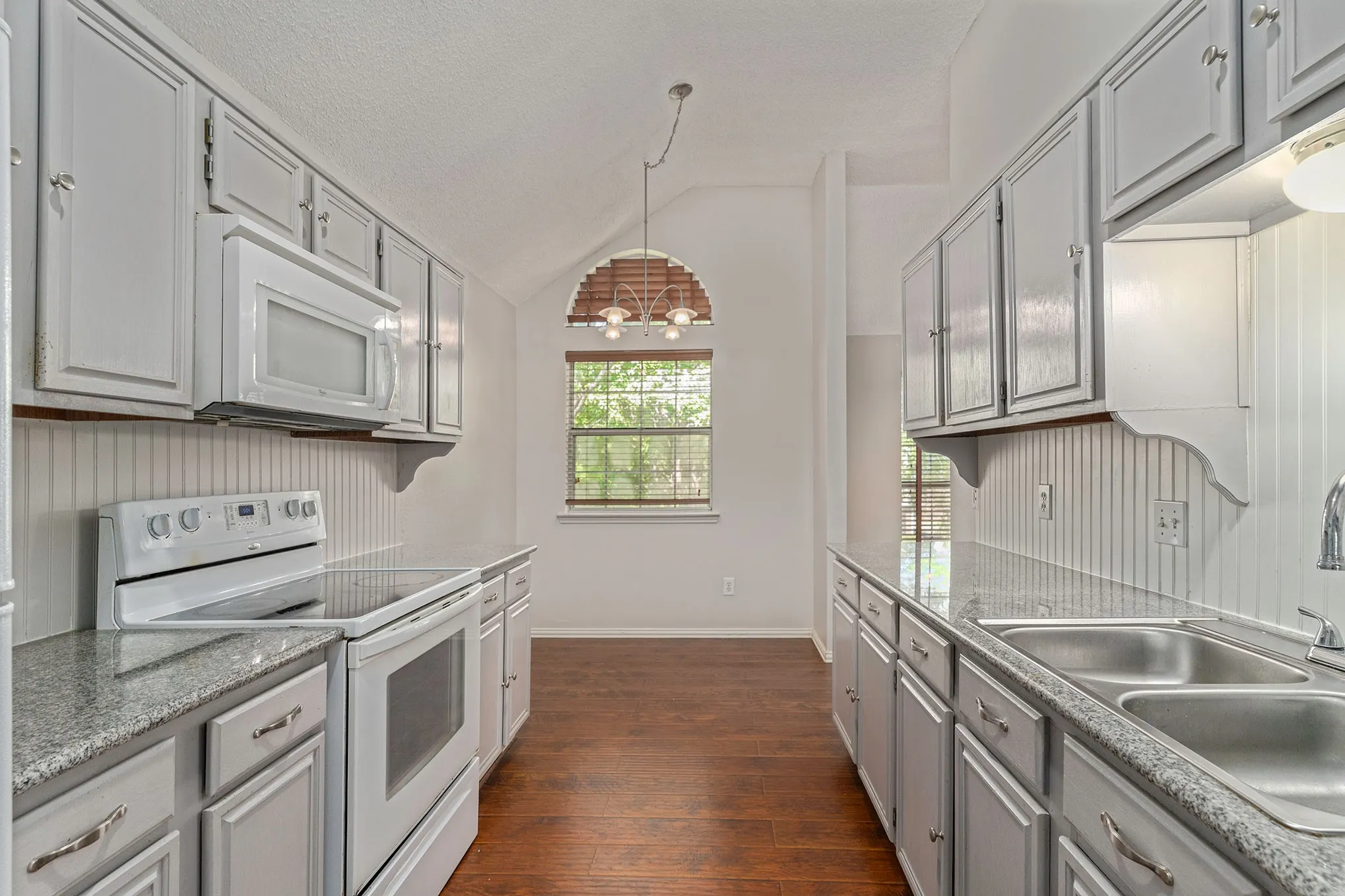 Kitchen with vaulted ceiling, gray cabinets, white appliances, dark wood-style floors, and a sink