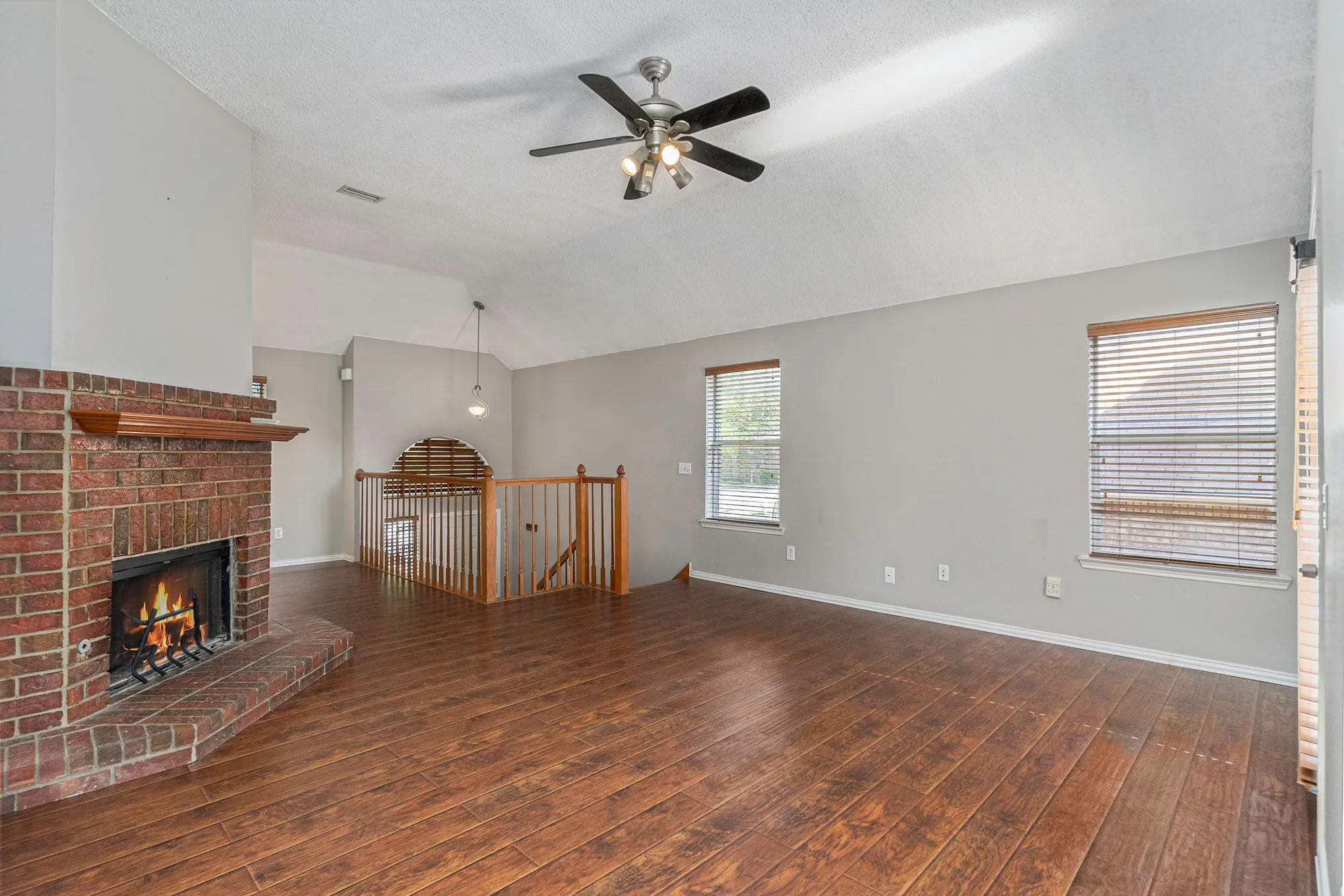 Unfurnished living room with a ceiling fan, visible vents, wood finished floors, a brick fireplace, and lofted ceiling