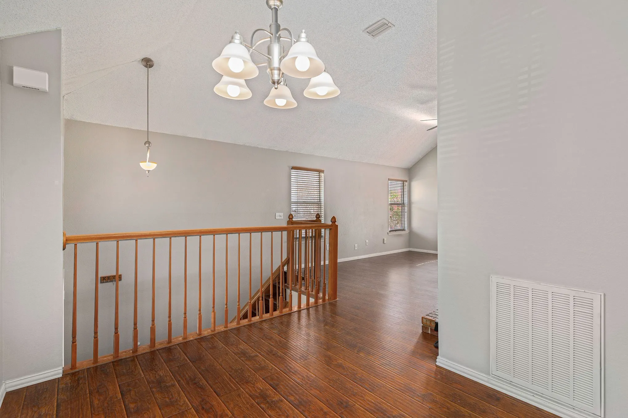 Hall featuring an inviting chandelier, an upstairs landing, visible vents, lofted ceiling, and hardwood / wood-style flooring