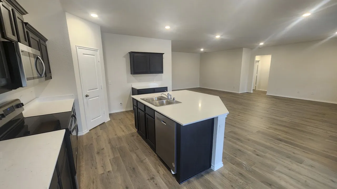 Open-concept kitchen featuring dark cabinetry, stainless steel appliances, and a central island with a dual sink and light-toned countertop