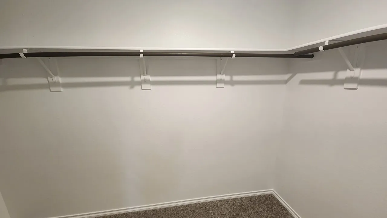 Walk-in closet featuring white walls, a single-tier rod and shelf system, and brown carpet flooring