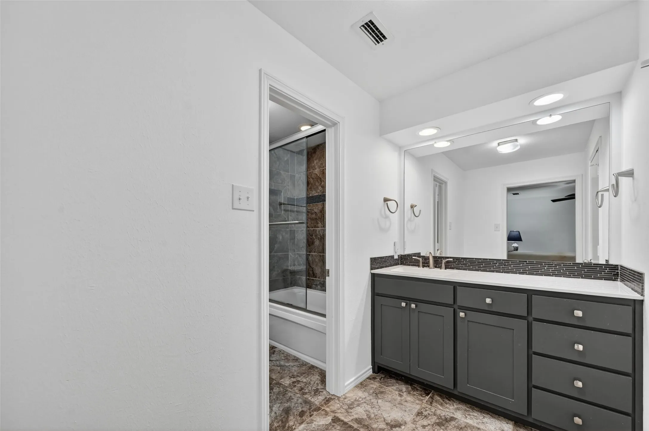 Bathroom featuring a dark gray vanity with brushed nickel hardware, white countertop, and a dark tile backsplash