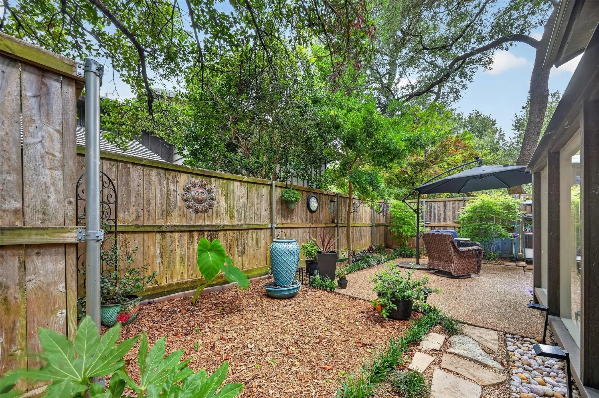 Private backyard oasis with a wood privacy fence, gravel patio area, wood chip landscaping beds, and mature trees
