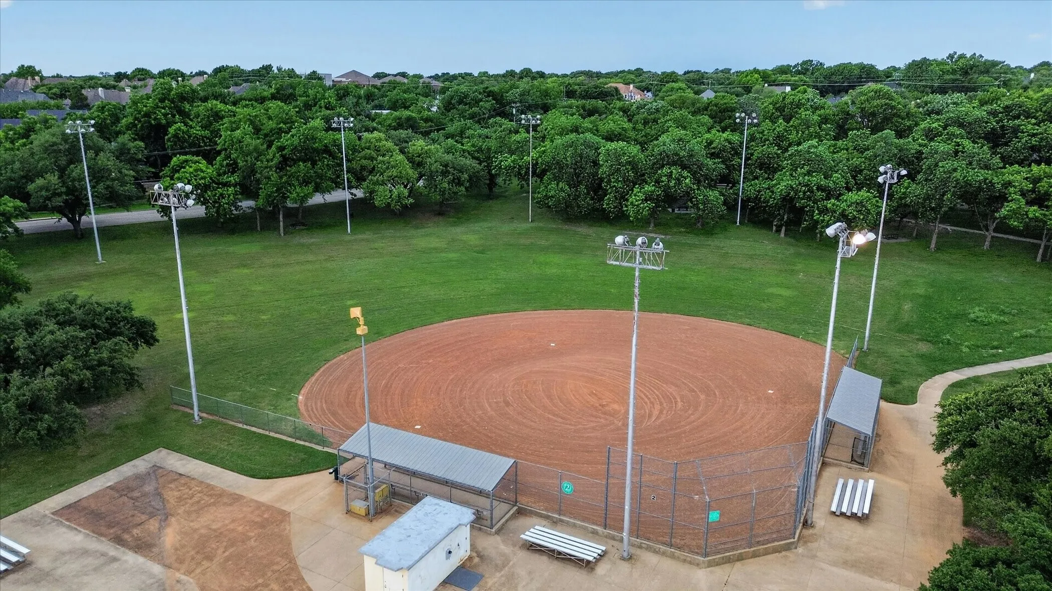 Baseball field featuring a red clay infield, surrounding green grass outfield, and a full set of stadium lights