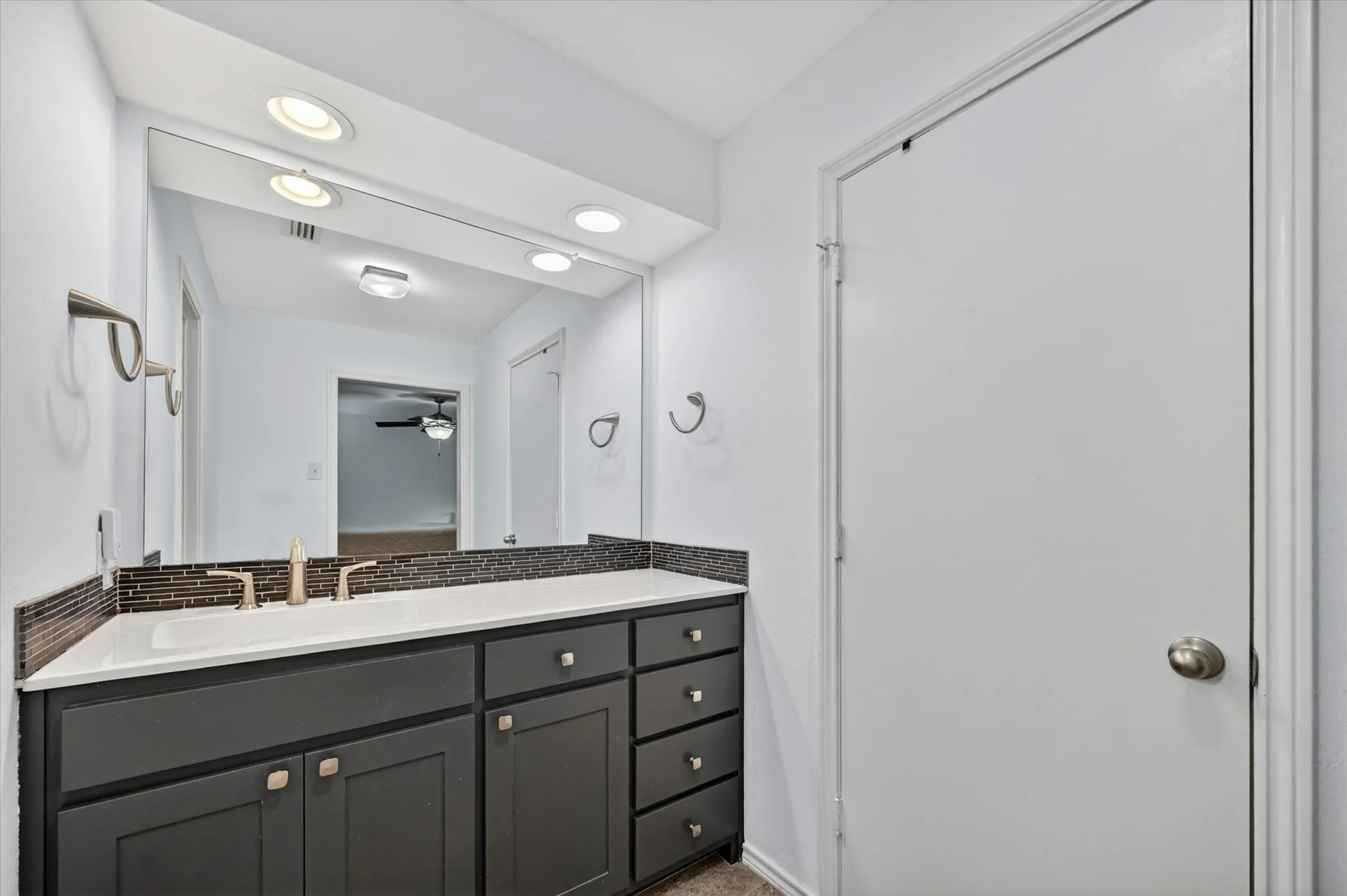 Bathroom vanity featuring dark cabinetry with brushed nickel hardware, a white countertop, and a mosaic tile backsplash