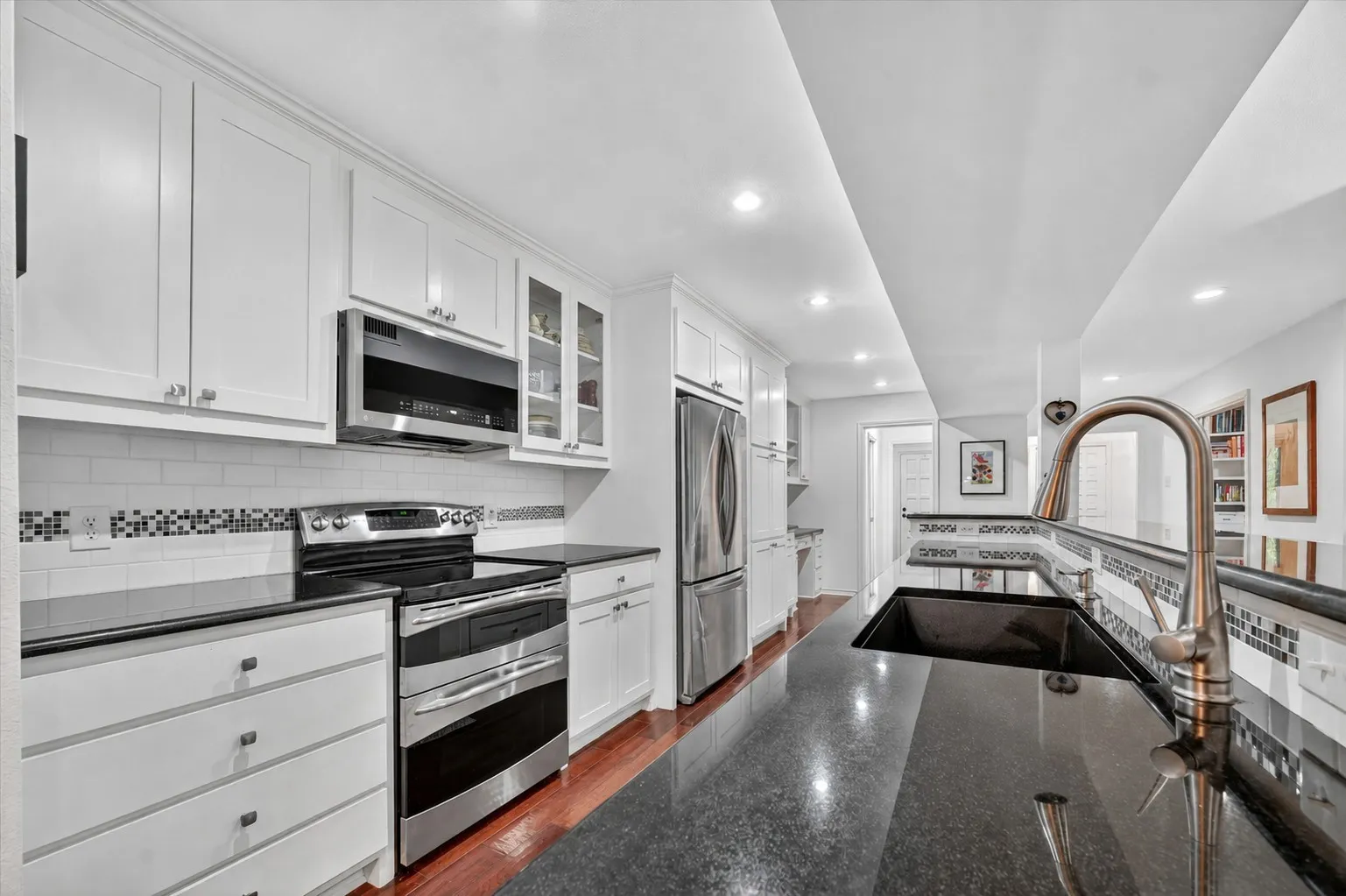 Modern kitchen featuring white cabinetry, black countertops, stainless steel appliances, a subway tile backsplash with decorative accent, and wood-finish flooring