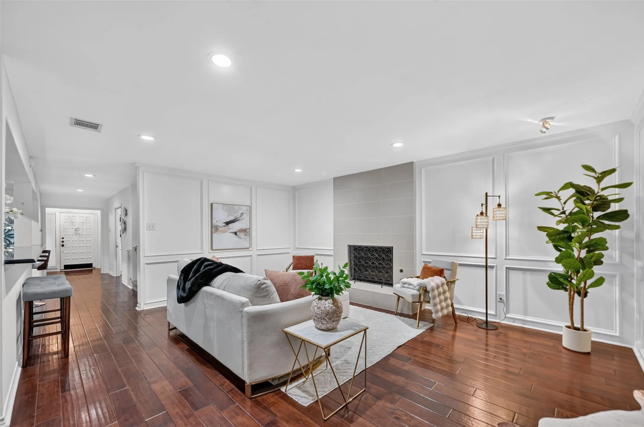 Hardwood flooring, recessed lighting, decorative wall paneling, tiled fireplace surround, and an intricate entry door