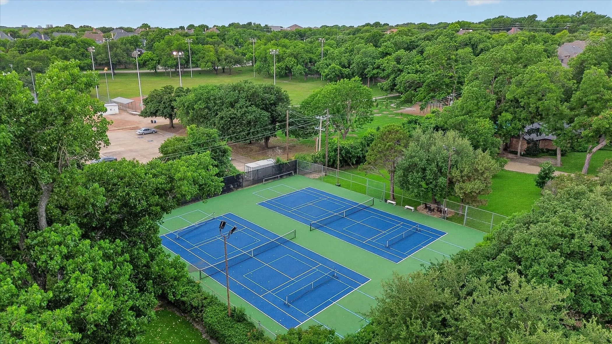 Two blue-surface tennis courts with green surrounding areas