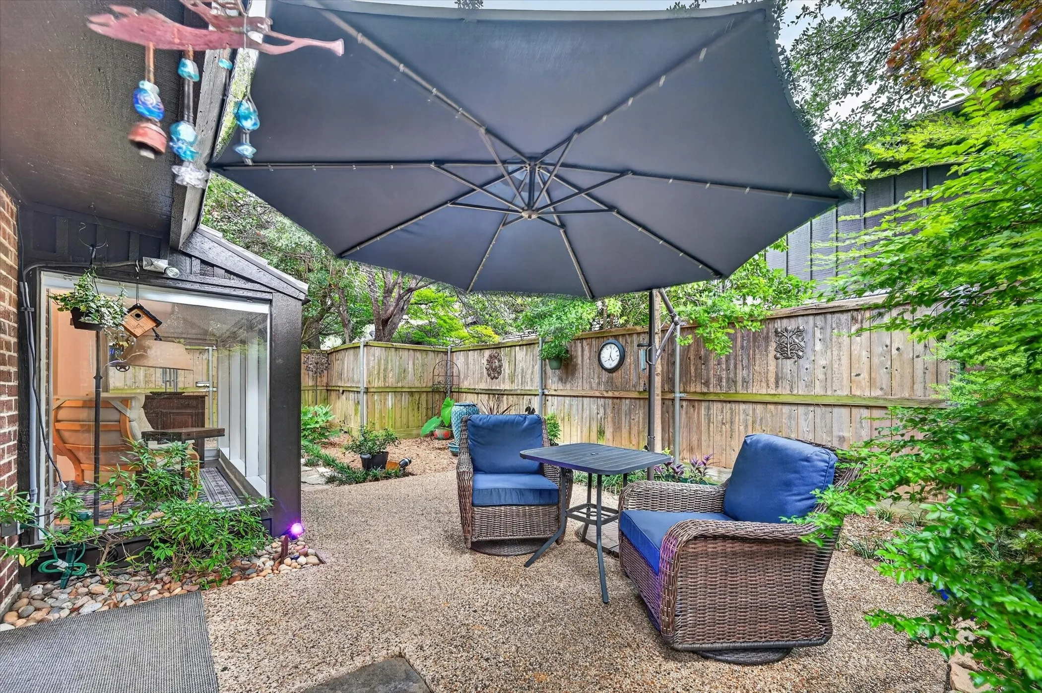 Private outdoor patio featuring a large umbrella, gravel surfacing, and a tall wood fence