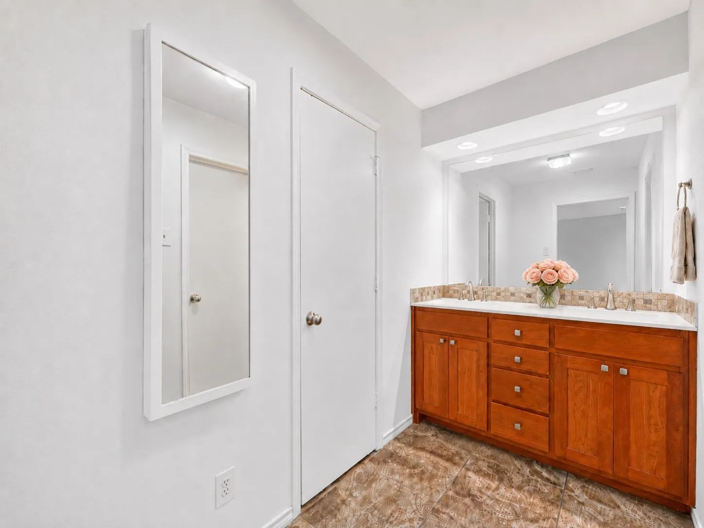 Dual vanity featuring wood cabinetry, white countertops, and a full-width mirror