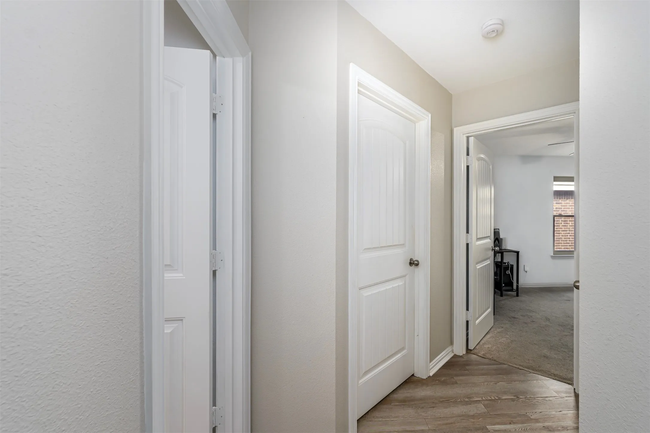 Corridor featuring light wood-style flooring, light carpet, and a textured wall