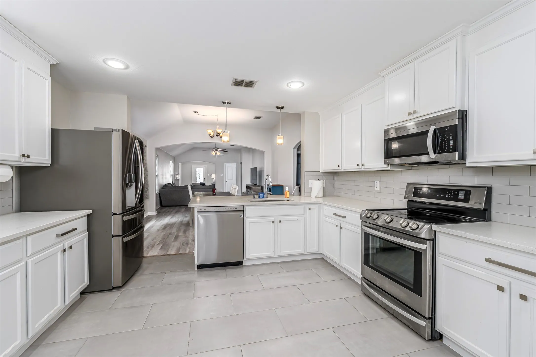 Kitchen featuring stainless steel appliances, open floor plan, arched walkways, white cabinets, and lofted ceiling
