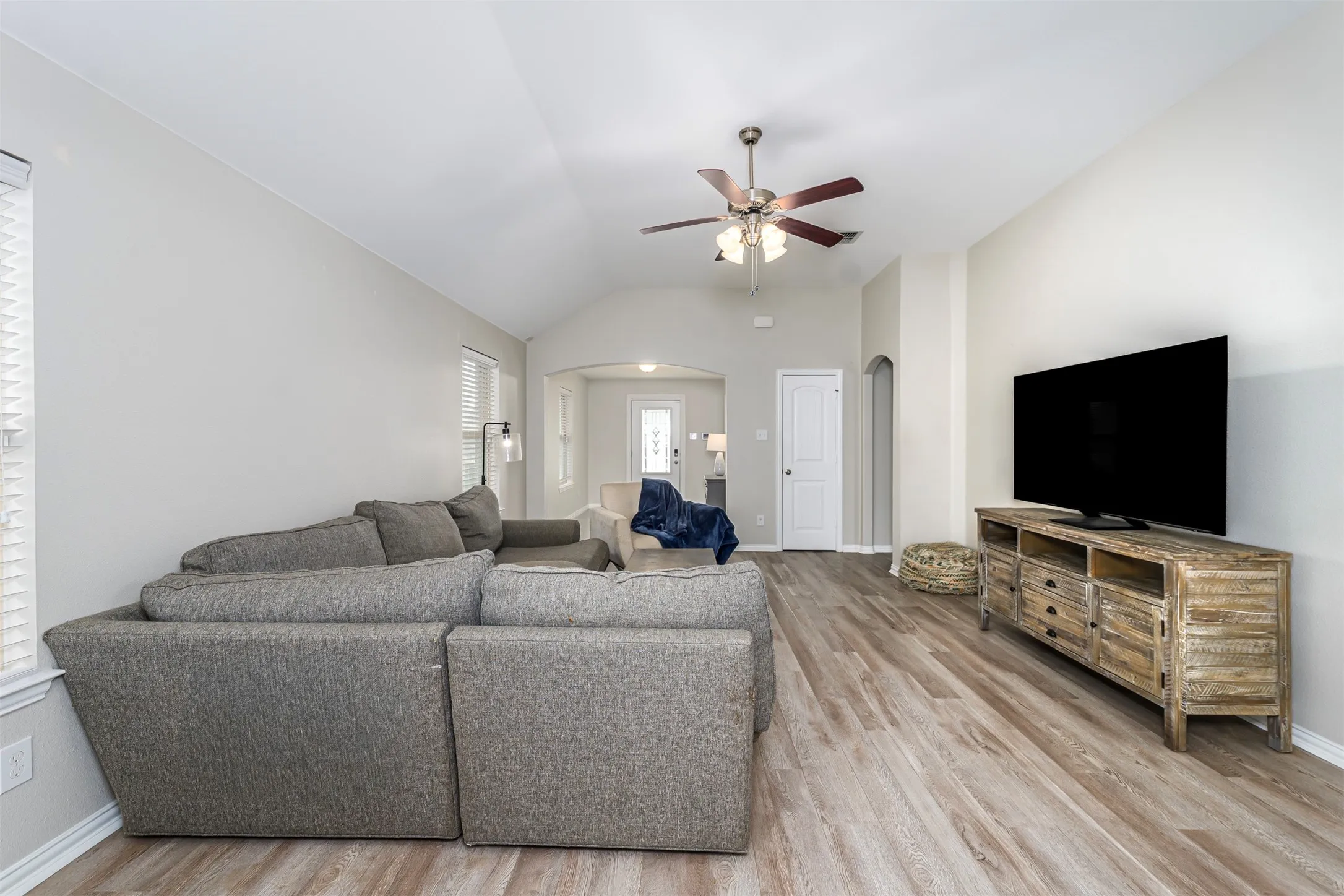 Living room with arched walkways, ceiling fan, light wood finished floors, and lofted ceiling