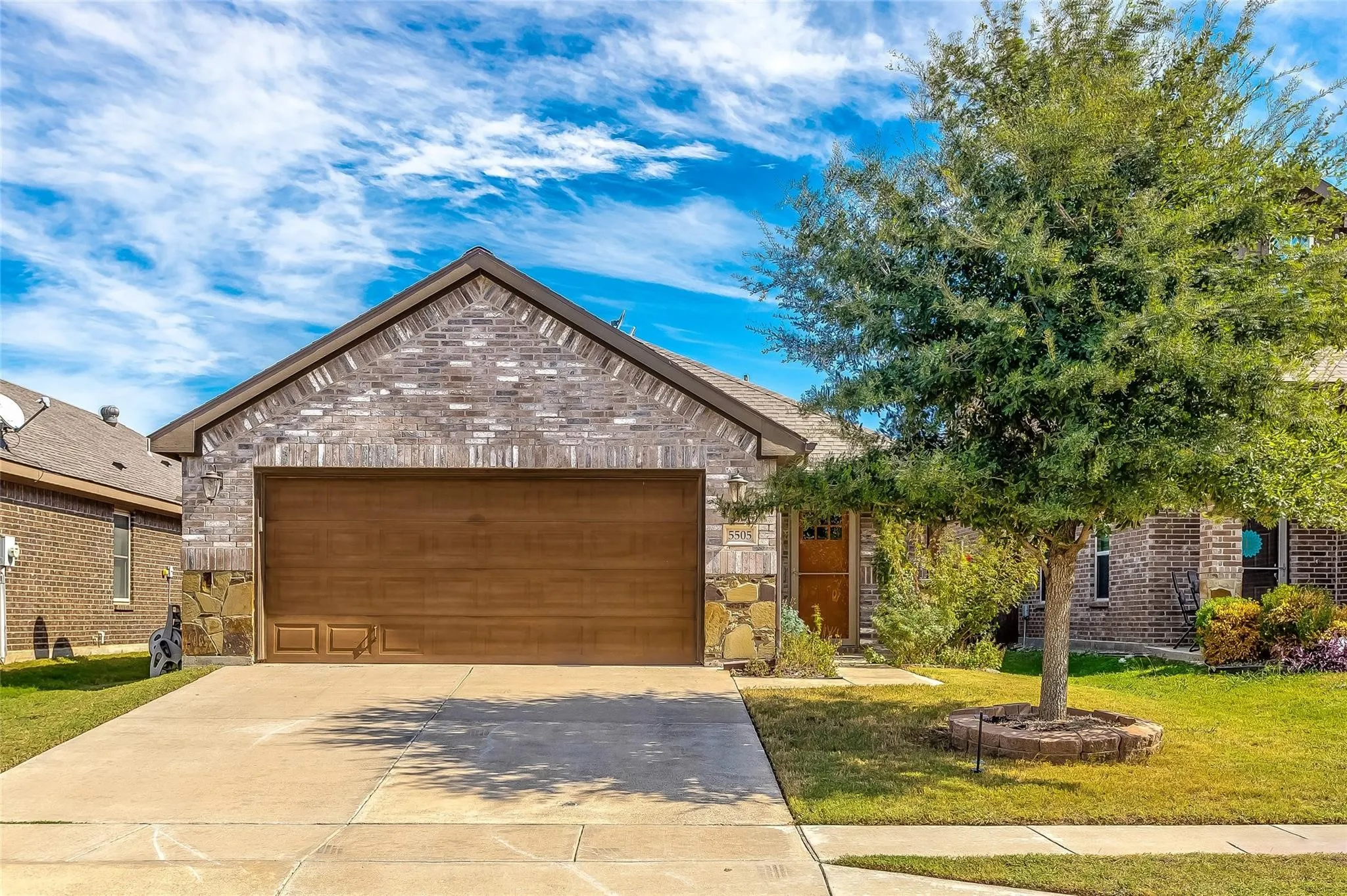 View of front facade featuring a front yard, concrete driveway, brick siding, an attached garage, and stone siding
