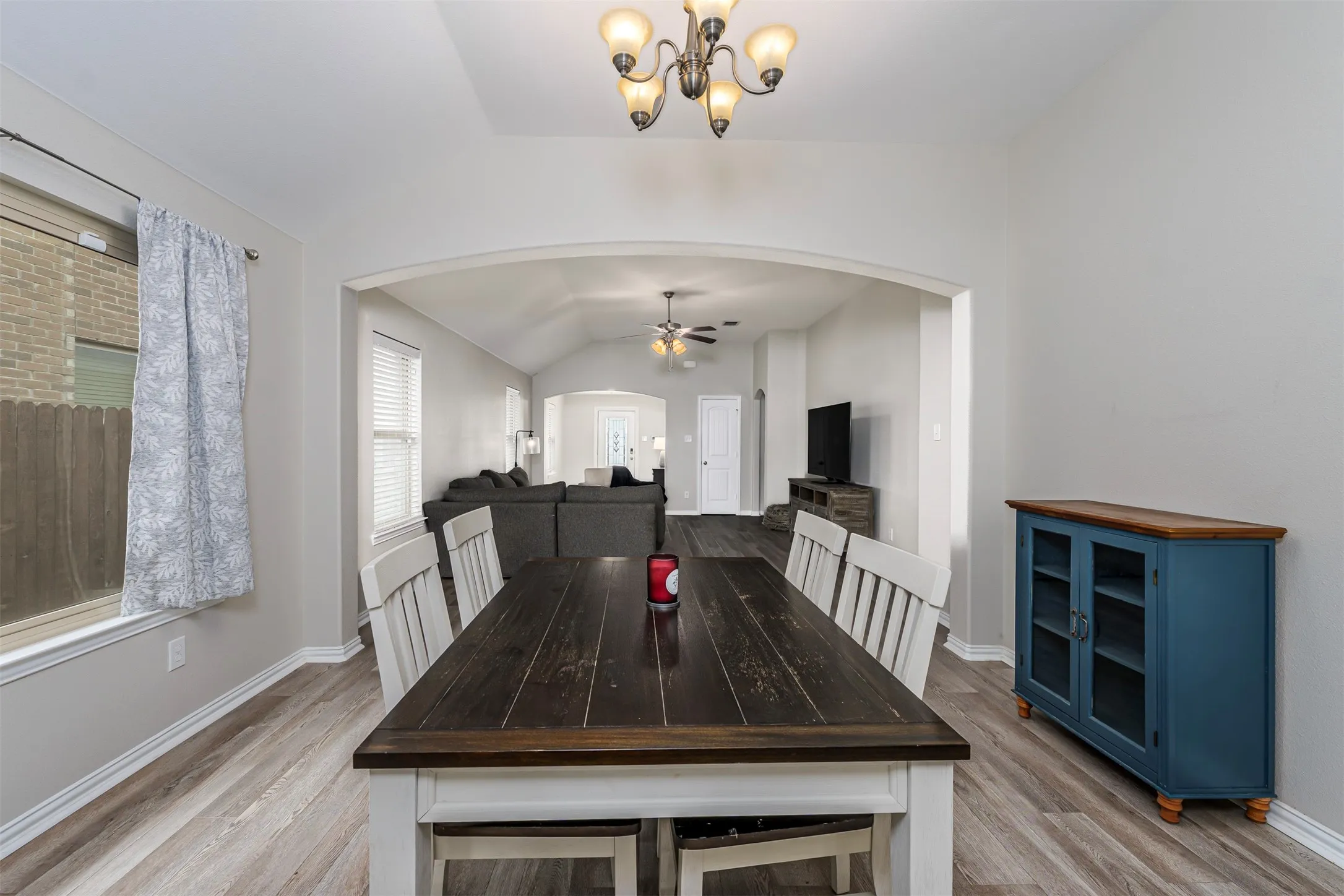 Dining area with lofted ceiling, arched walkways, light wood-style flooring, ceiling fan, and a chandelier