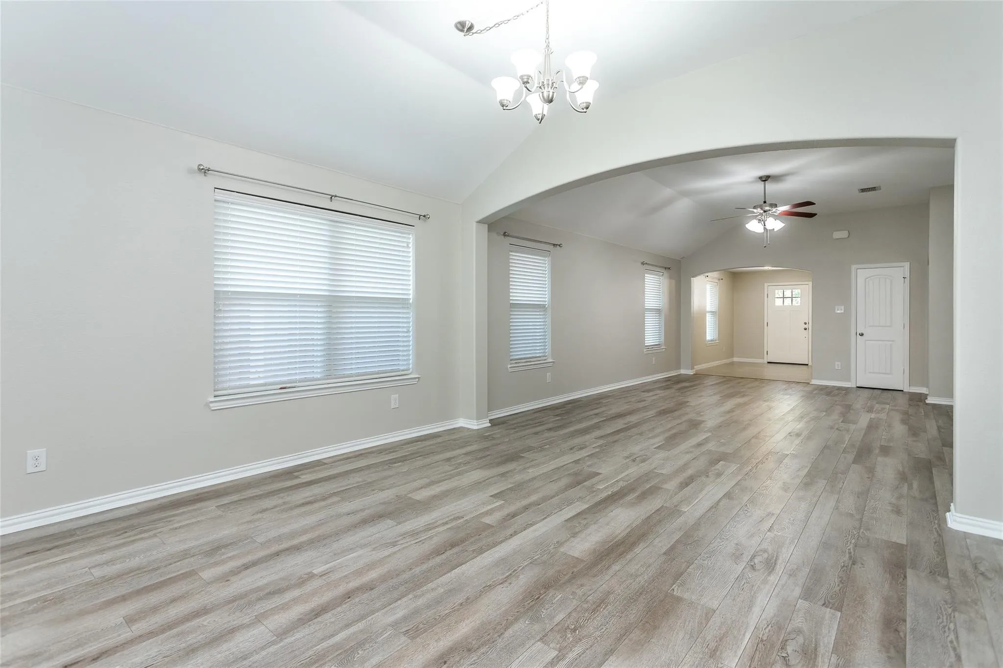 Unfurnished living room featuring light wood-style flooring, ceiling fan, arched walkways, lofted ceiling, and hanging lights