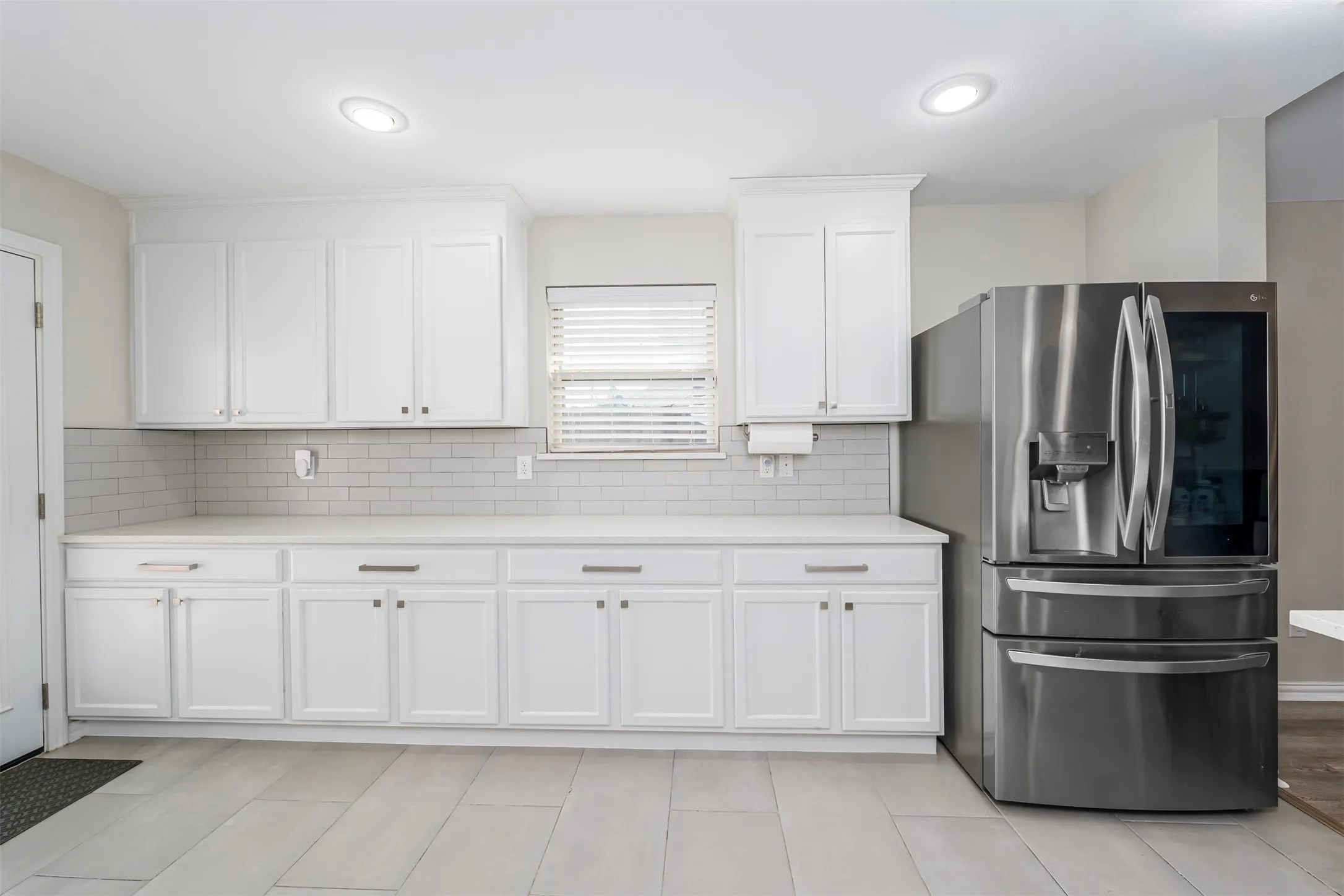 Kitchen with stainless steel refrigerator with ice dispenser, white cabinets, decorative backsplash, and light stone countertops