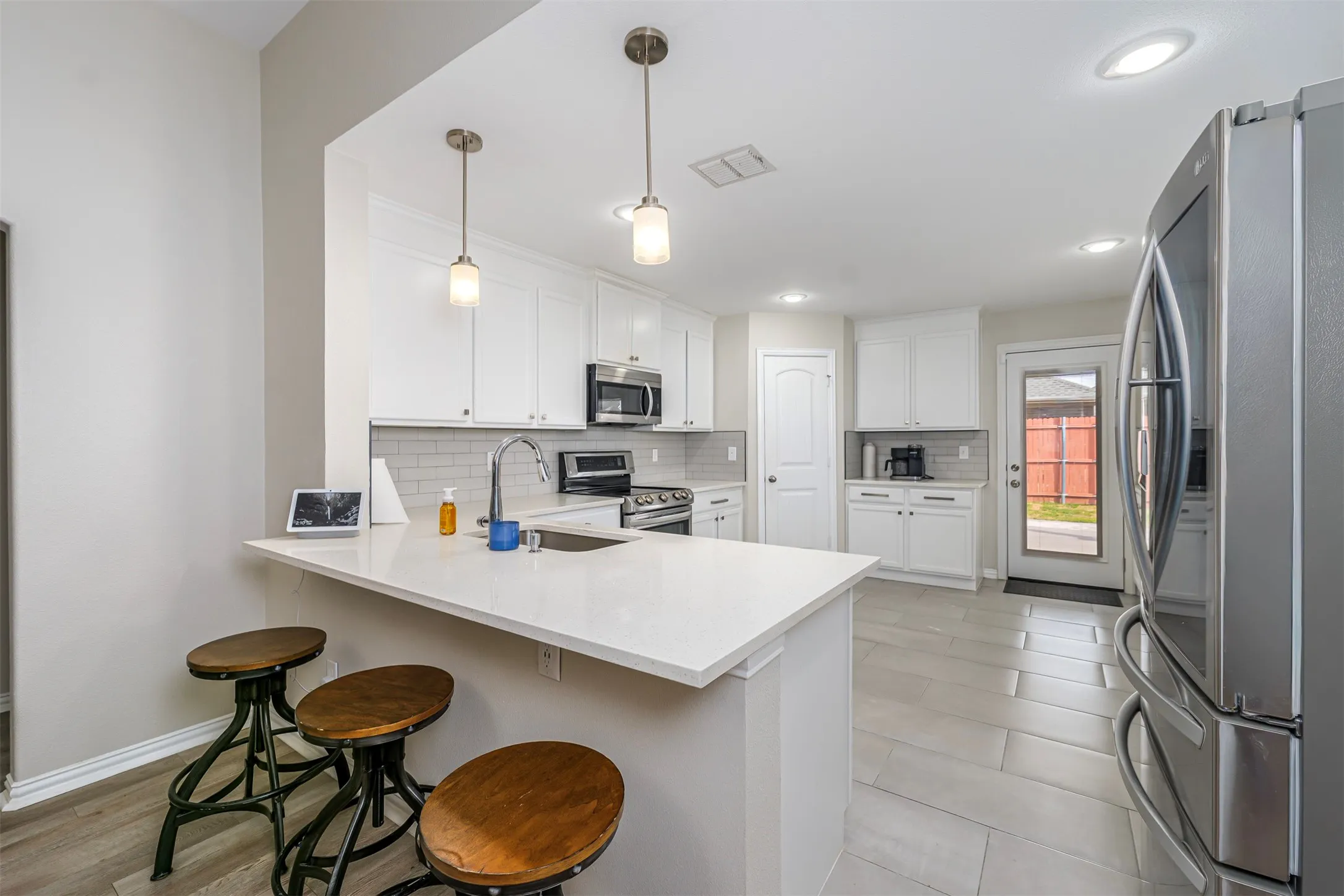 Kitchen featuring stainless steel appliances, a peninsula, a kitchen breakfast bar, white cabinets, and pendant lighting