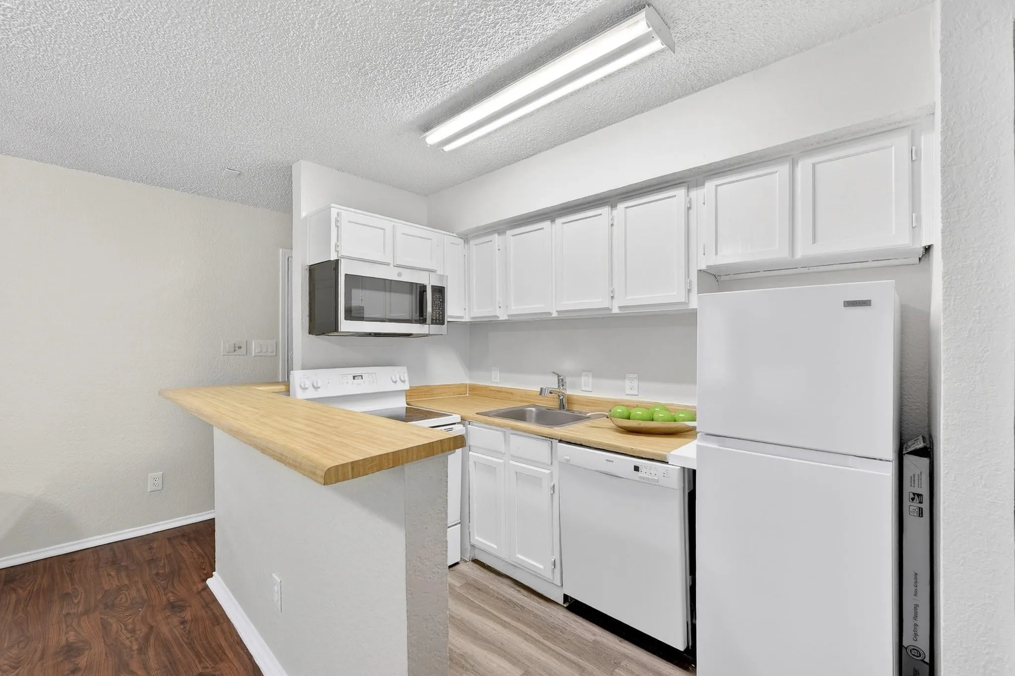 Kitchen featuring white cabinetry, light wood-finish countertops, stainless steel over-the-range microwave, and white appliances including a refrigerator, range, and dishwasher