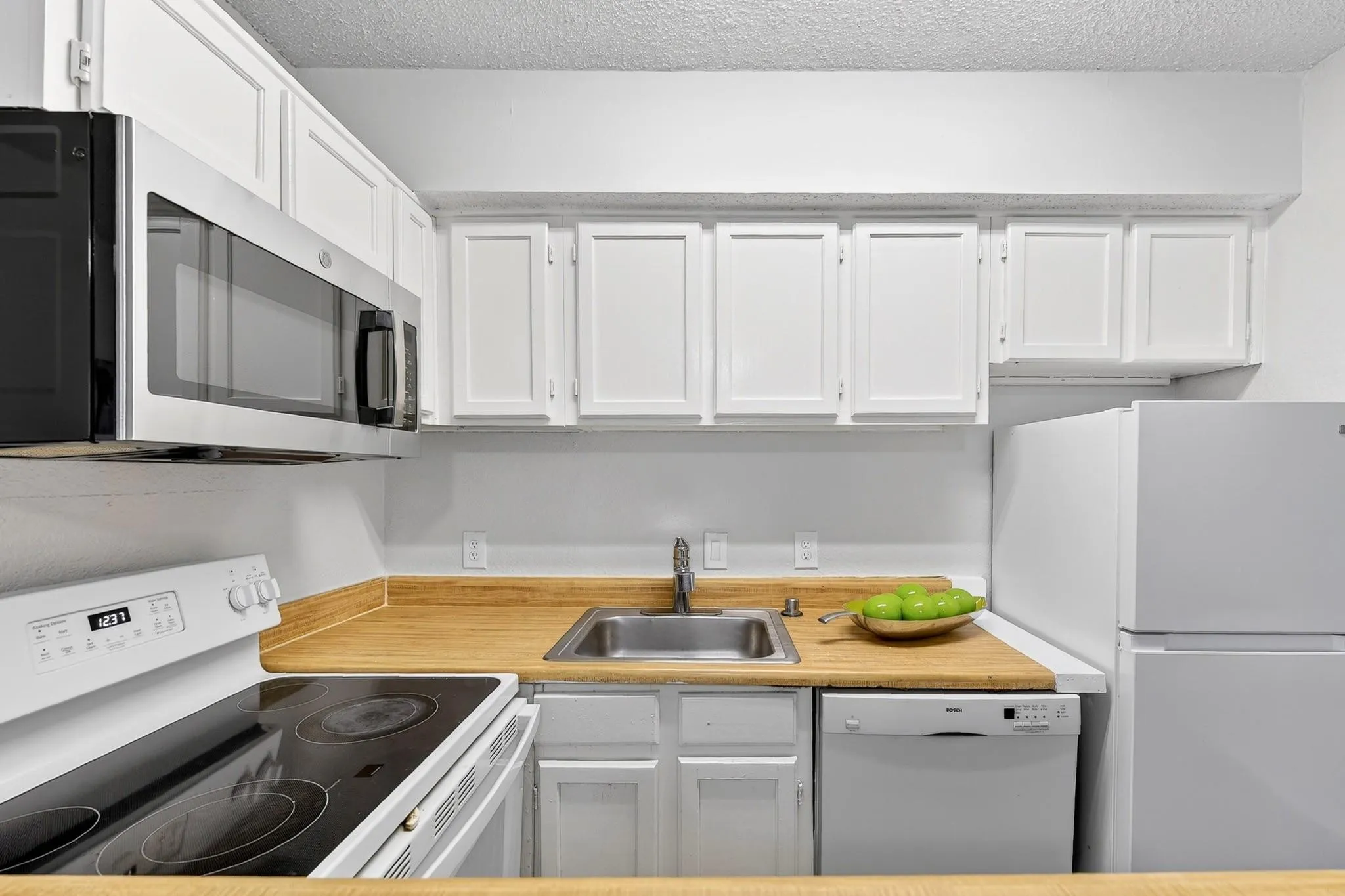 Kitchen featuring white cabinetry, wood-finish countertops, stainless steel microwave, and white appliances including a refrigerator, range, and dishwasher