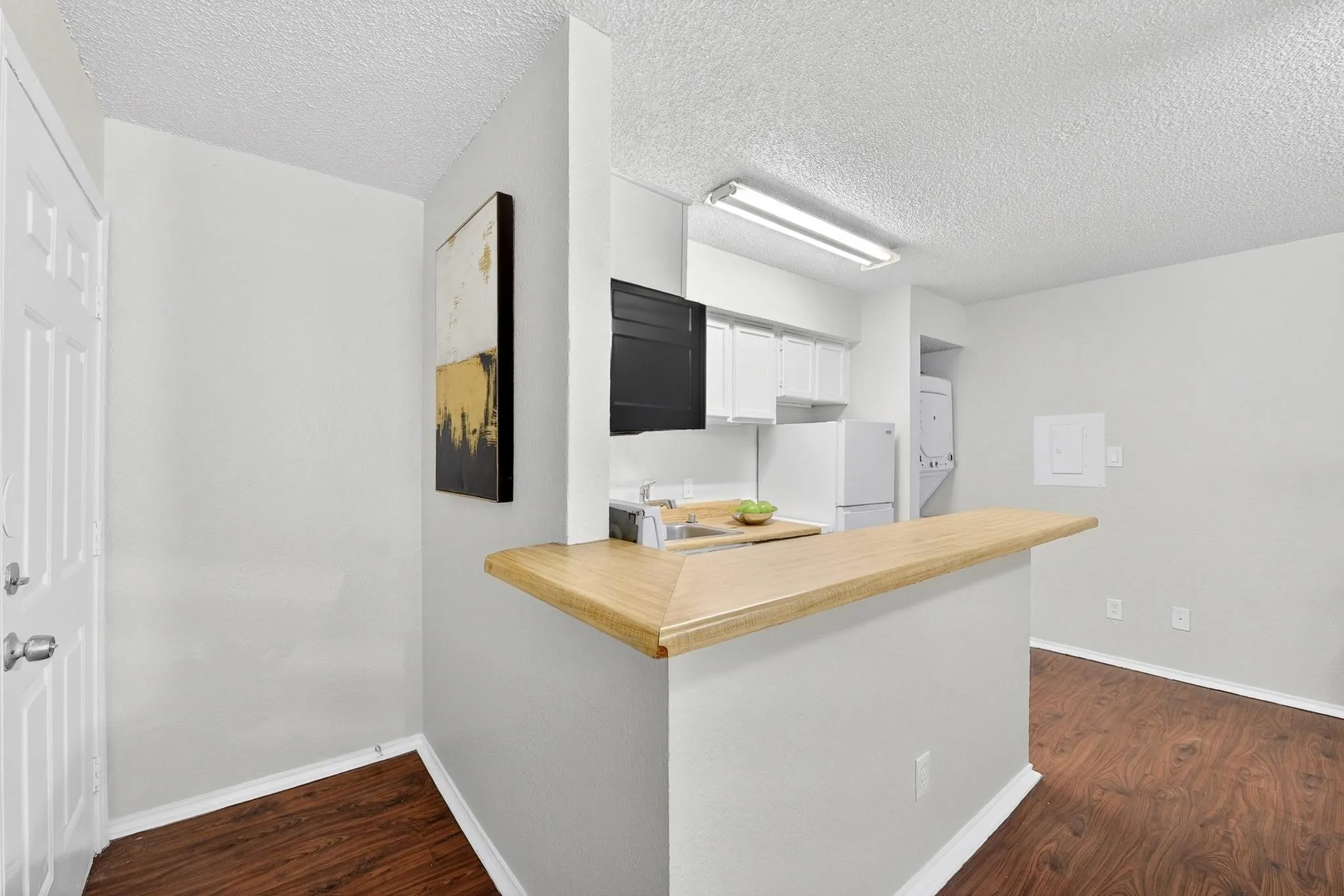 Kitchen area featuring wood-finish flooring, white cabinetry, a built-in breakfast bar with a wood-finish countertop, and a white appliance package