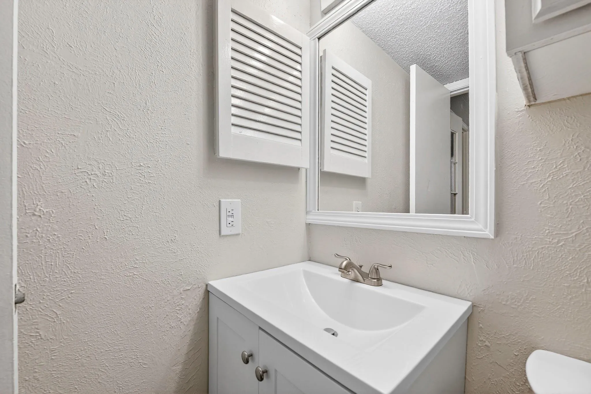 Bathroom vanity featuring a white cabinet, integrated sink, brushed nickel faucet, and framed mirror