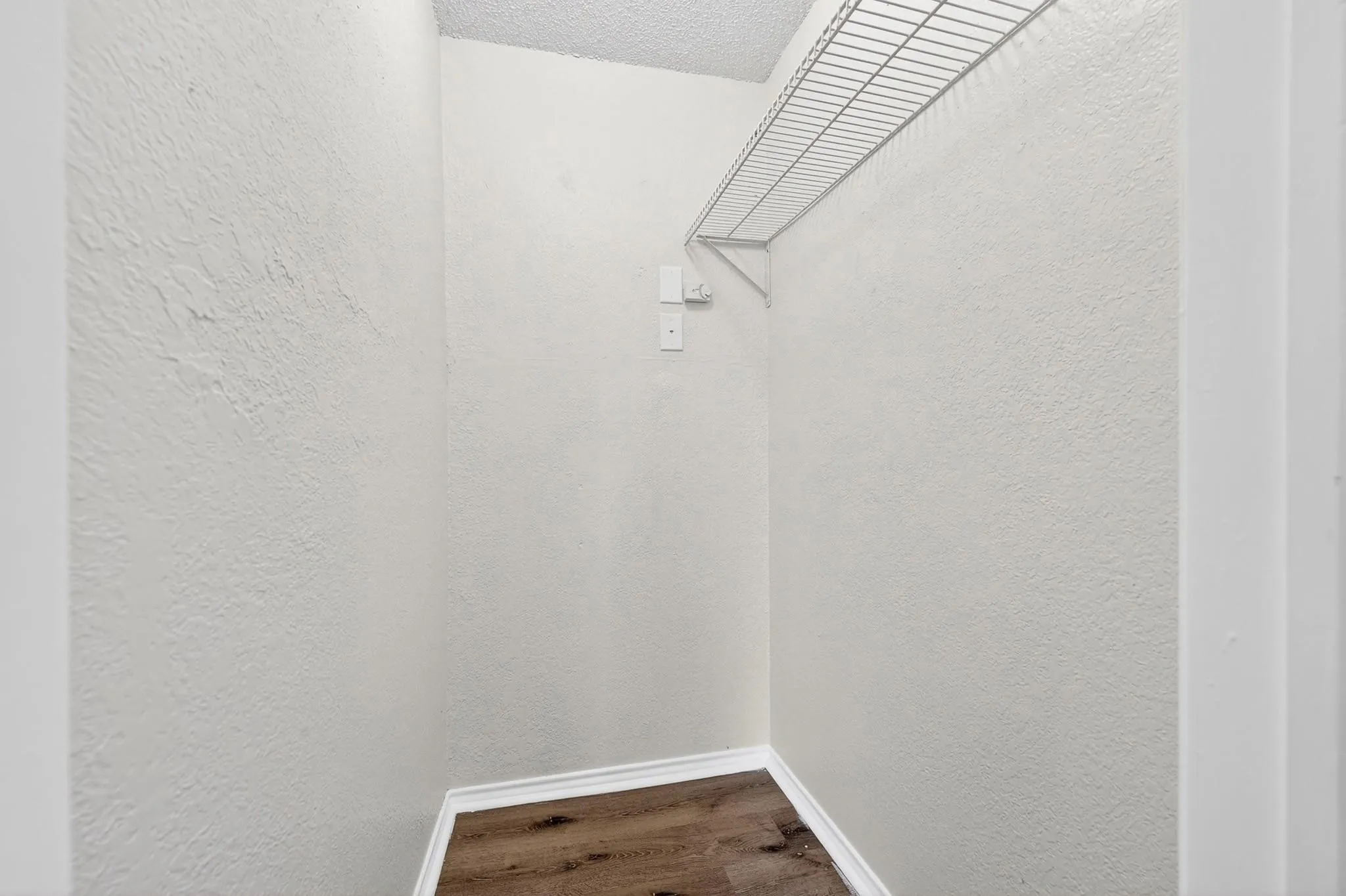 Compact storage area featuring wood-finish flooring, white baseboards, and a wire shelving unit