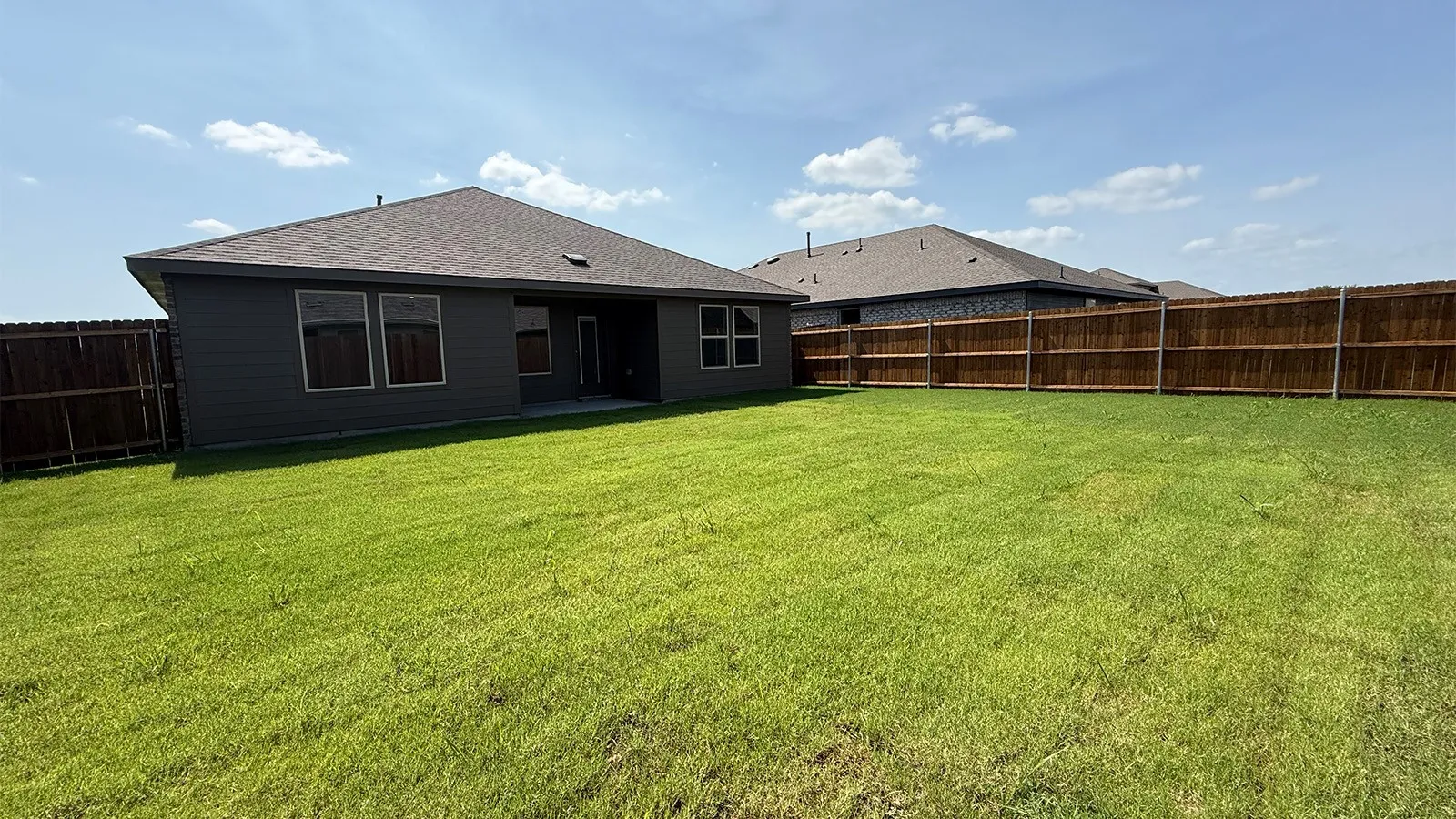 Expansive backyard featuring a manicured lawn, dark wood privacy fencing, and a concrete patio