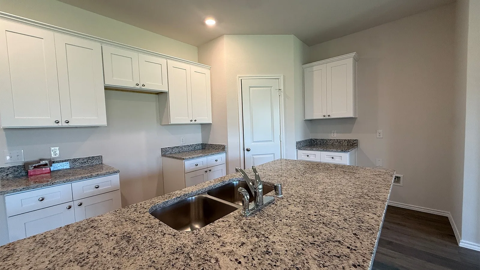 Kitchen featuring a large island with a double stainless steel sink and chrome faucet, granite countertops, white cabinetry with silver hardware, and wood-finish flooring