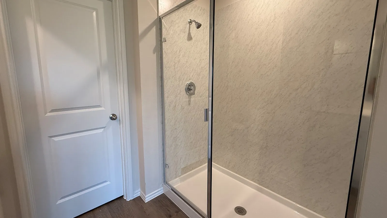 Shower enclosure with glass paneling, a white shower base, and textured wall surrounds