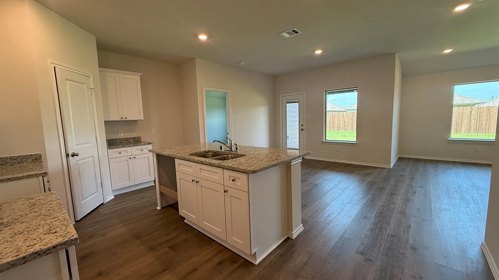 Spacious kitchen featuring an island with a double basin sink, white cabinetry, and granite countertops