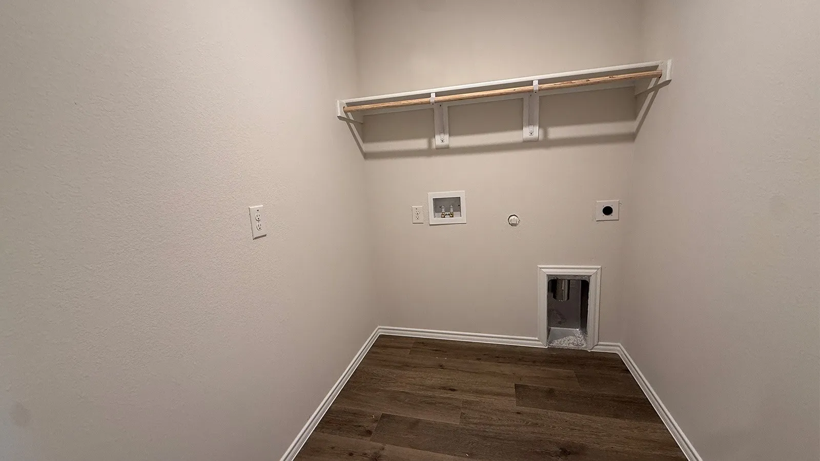 Dedicated laundry area featuring a wood-finish flooring, light-toned walls, white baseboards, and an integrated clothes rod with shelving