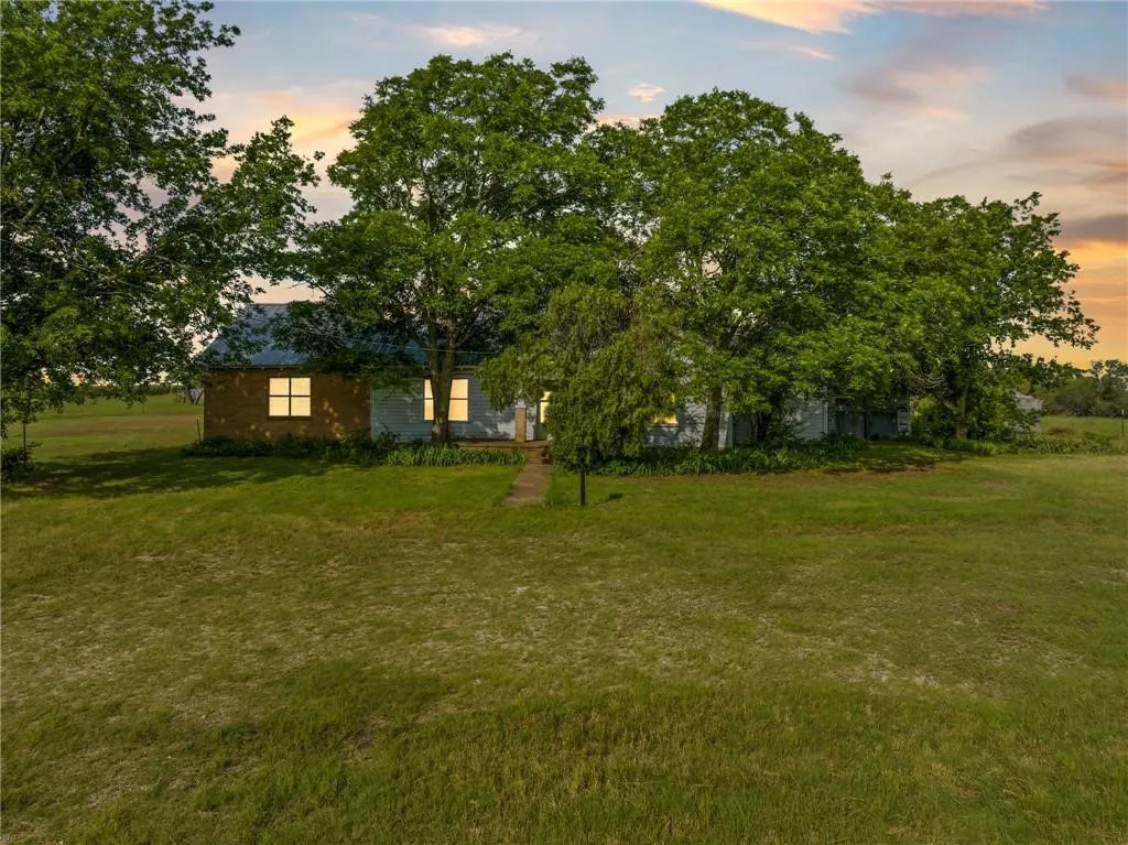 Single-story residence featuring a brick and siding exterior, a light-colored metal roof, and multiple mature trees providing shade