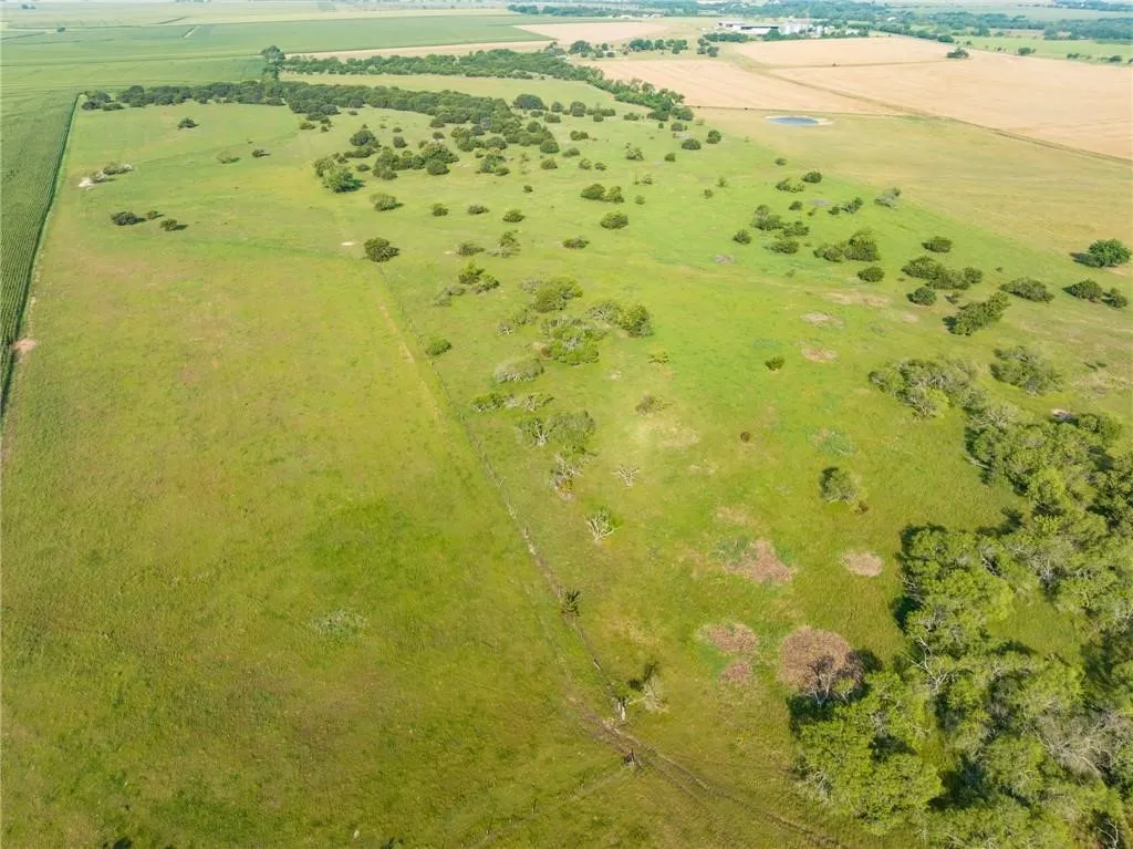 Expansive acreage featuring open green fields, scattered trees, and a distant agricultural landscape