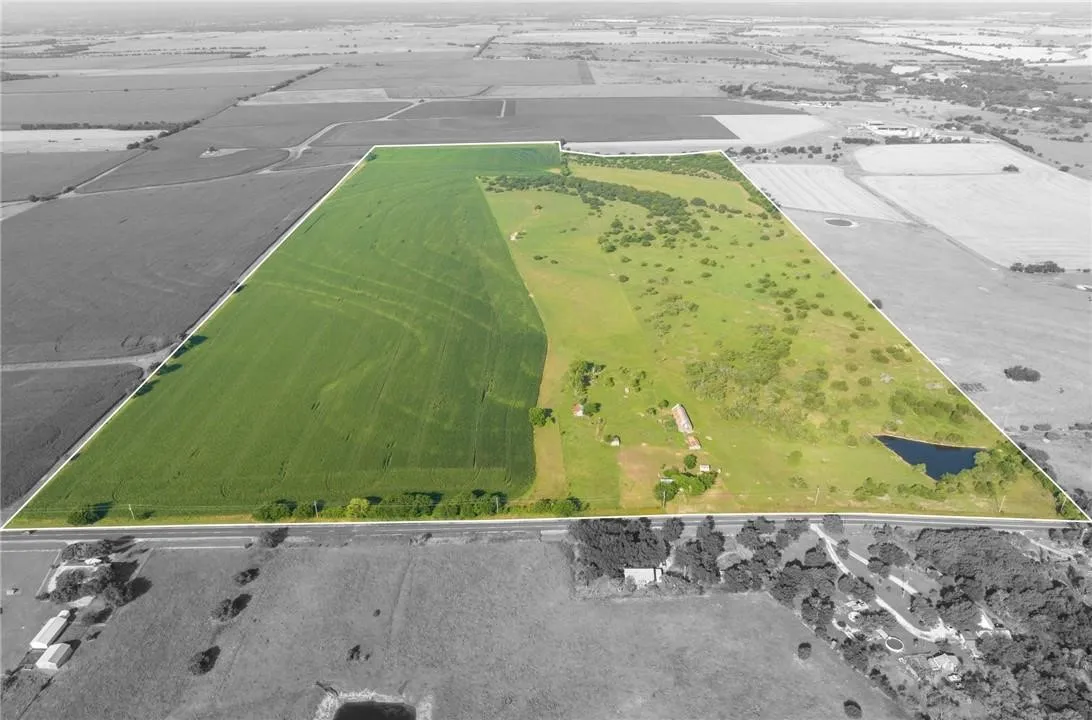Expansive agricultural parcel featuring a cultivated field, open pastureland, a natural pond, multiple structures, and direct road frontage