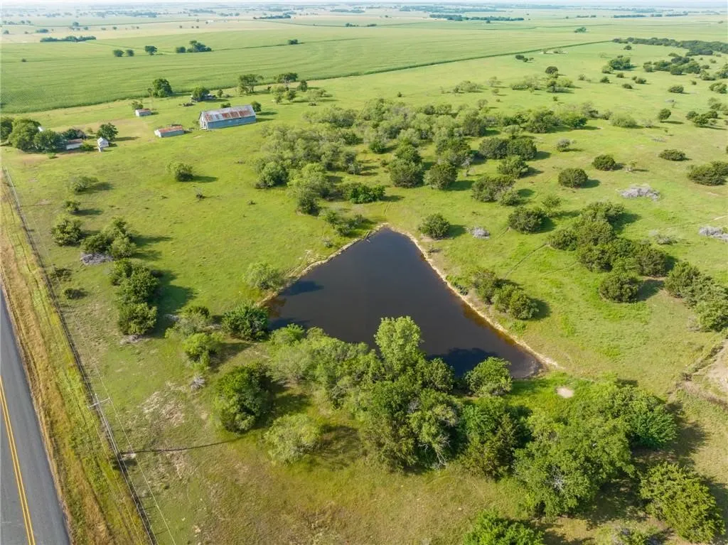 Expansive rural property featuring a large pond, a two-lane paved road frontage, established structures including a barn and outbuildings, and abundant green space with scattered trees