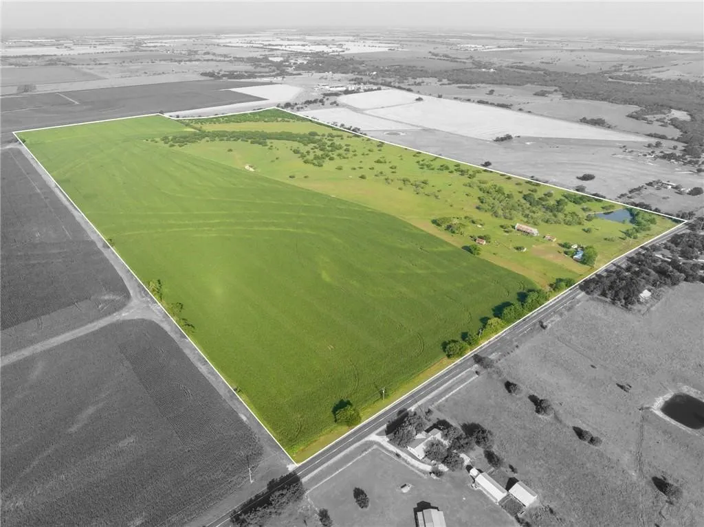 Expansive agricultural property featuring a substantial cultivated field, natural tree lines, a private pond, and multiple structures