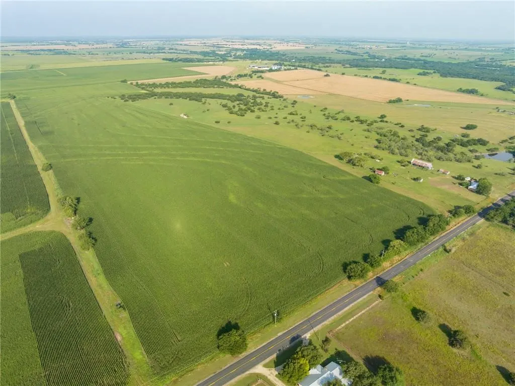 Expansive agricultural land featuring cultivated fields, a paved roadway bordering the property, scattered trees, and distant rural structures