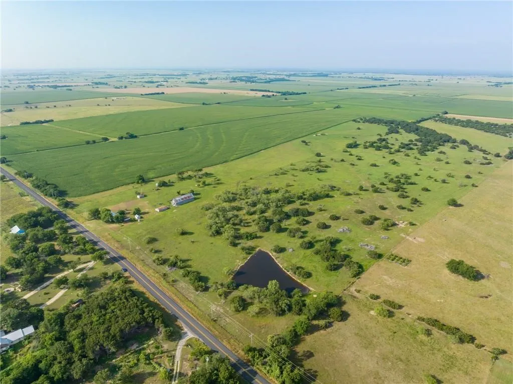 Expansive rural landscape featuring a private pond, open pastures, agricultural fields, a main road frontage, and several outbuildings