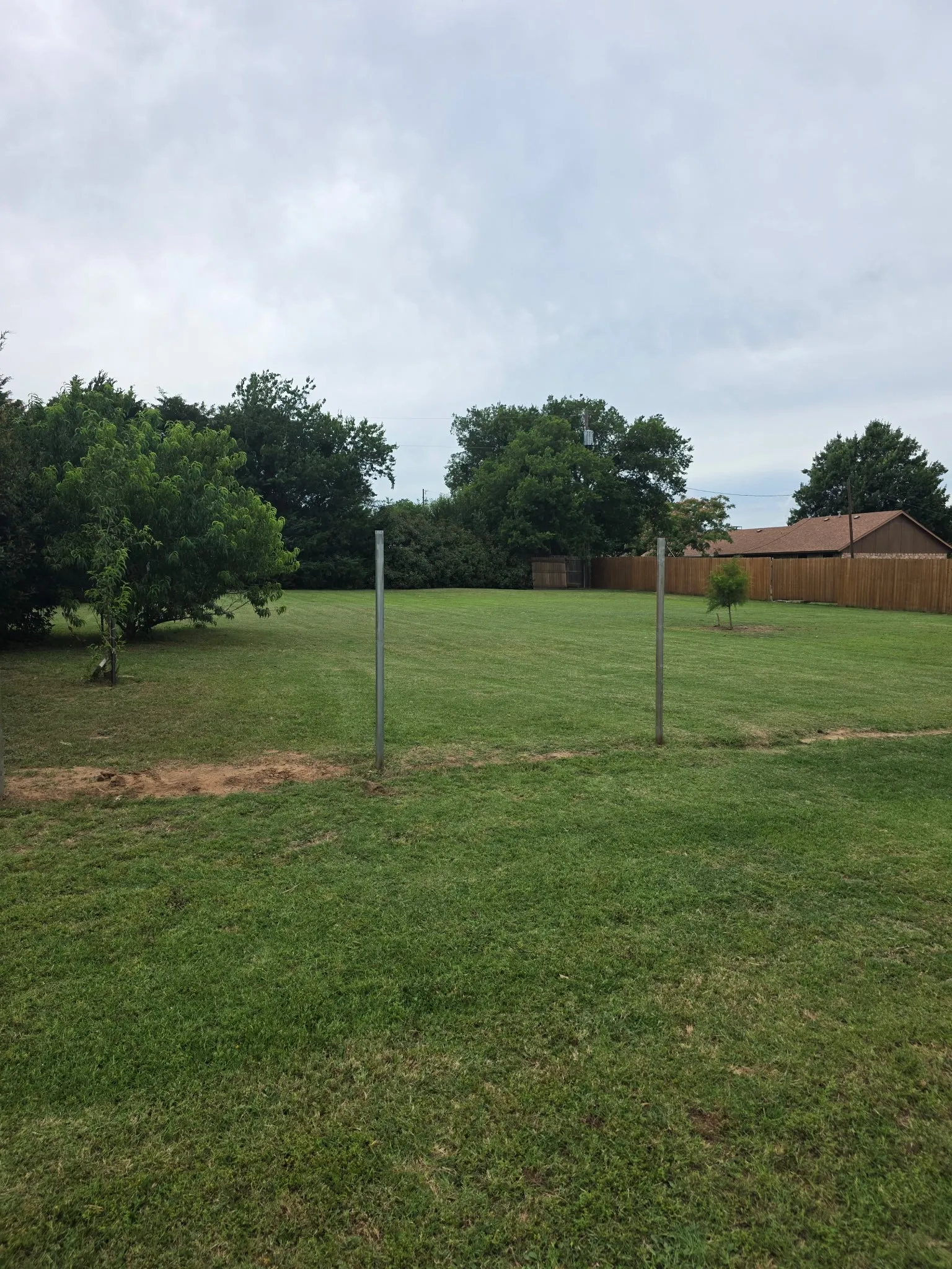 Expansive grassy area featuring mature trees and a wood fence border